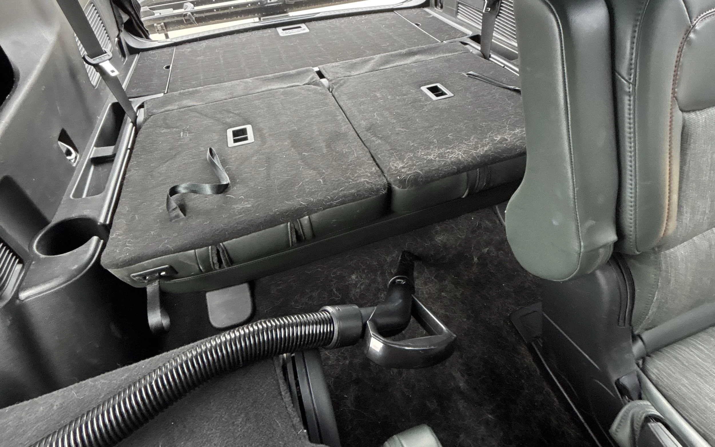 The interior of a vehicle with the second row folded down, revealing the cargo space, with a latch and a vacuum hose visible.
