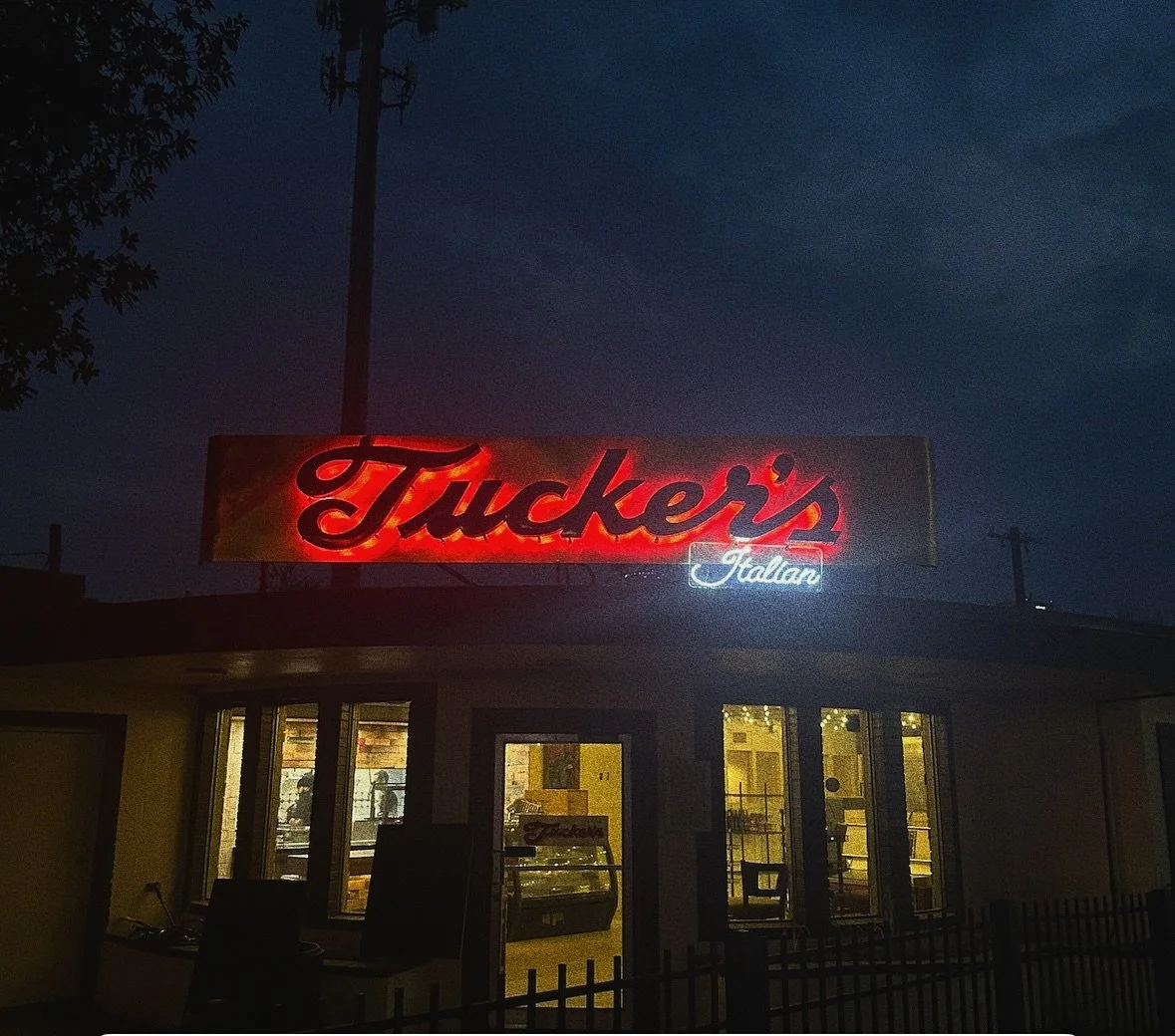 Neon sign for Tucker's Italian restaurant at night, with lit interior visible through windows and a dark sky