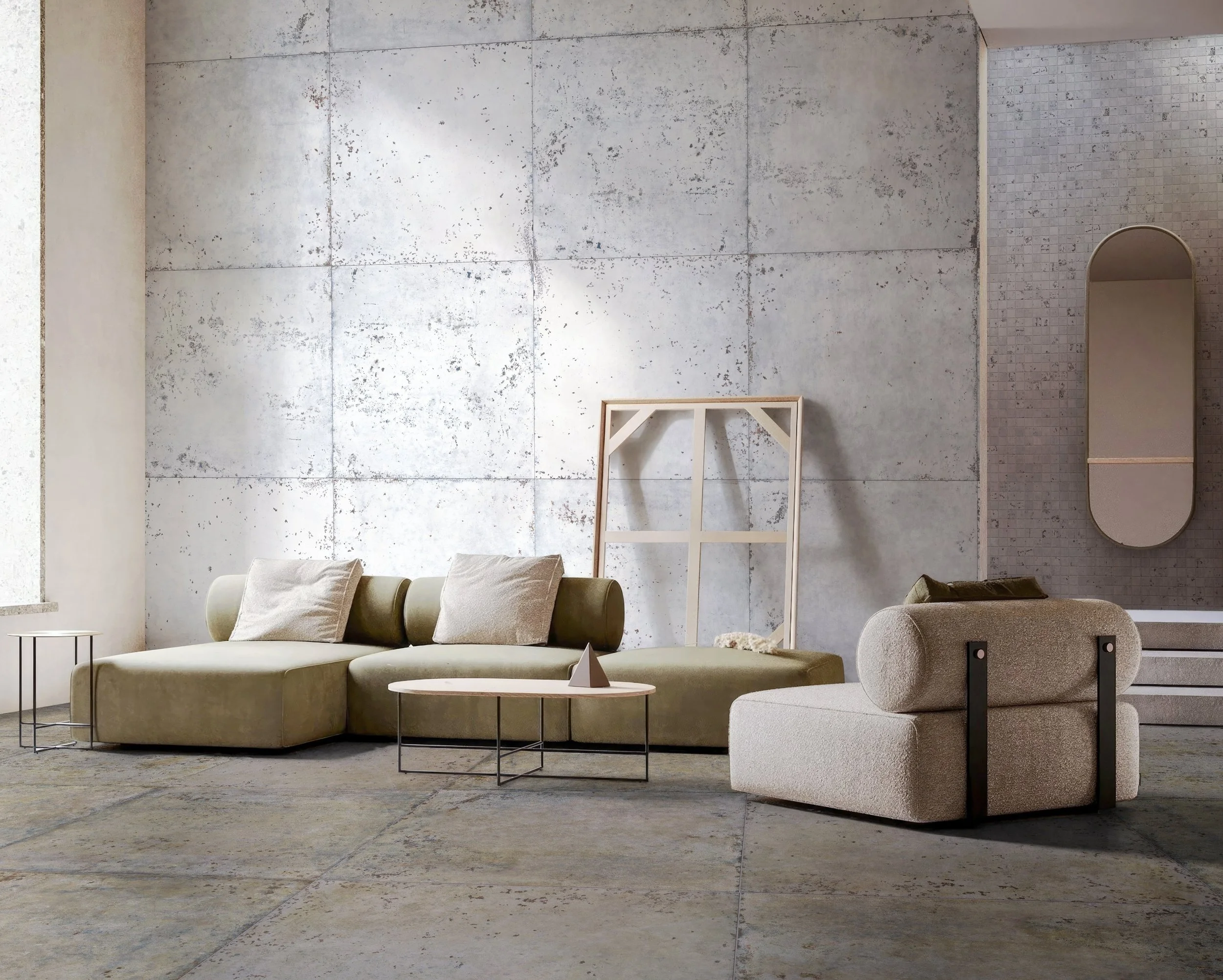 Modern living room with minimalist furniture, including a green sectional sofa, a beige armchair, and small side tables, set against a textured gray wall with a window on the left.