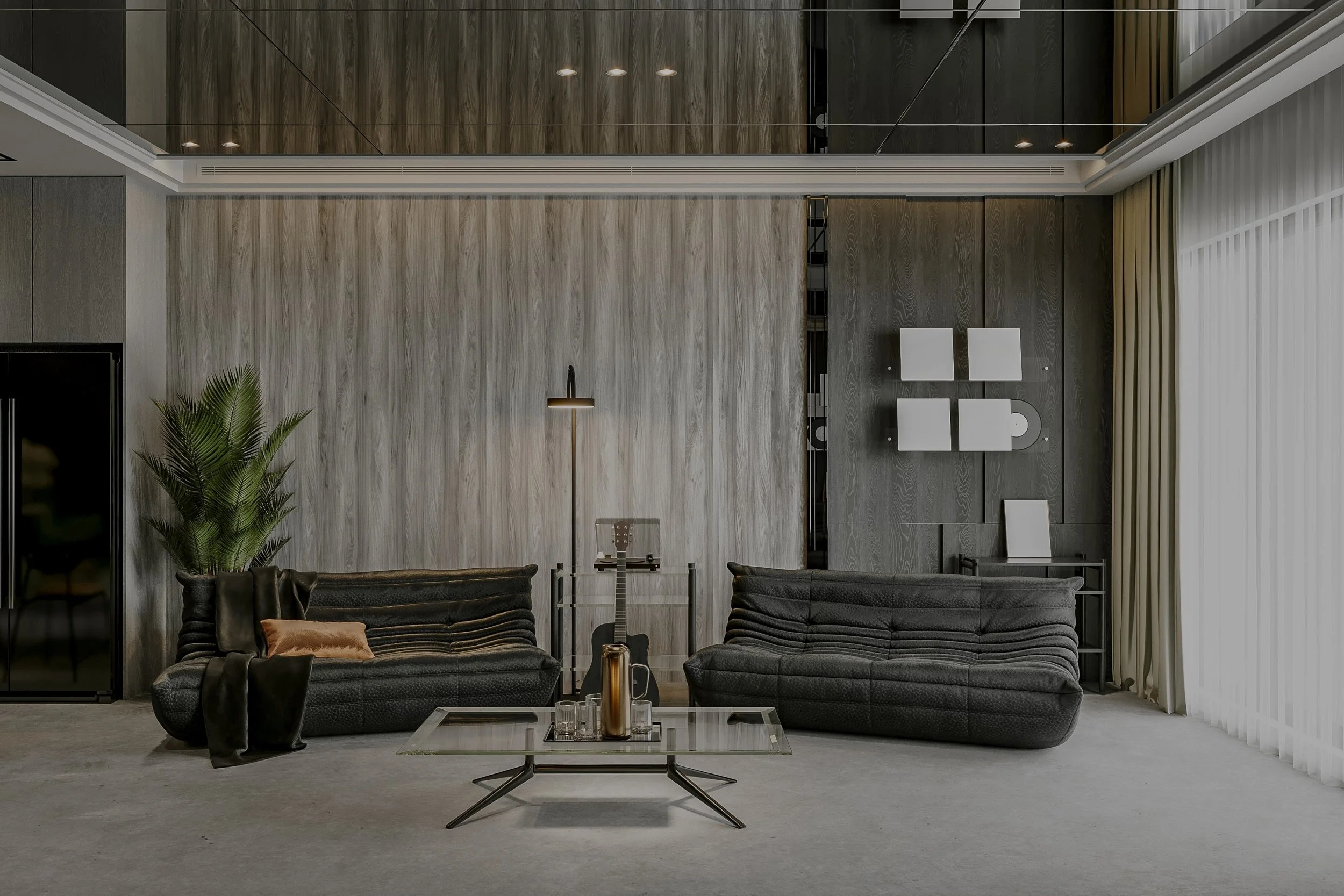 Modern living room with two black sofas, glass coffee table with decorative objects, tall green plant, wall-mounted art, and a large window with sheer curtains.
