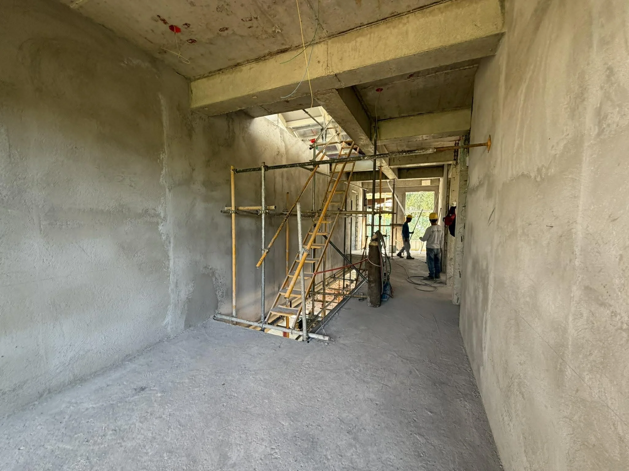 Construction workers inside a building under construction, with scaffolding, ladders, and raw concrete walls.