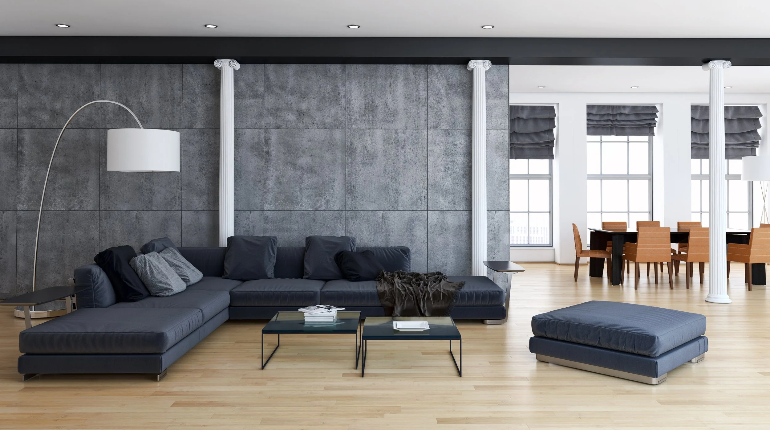 Modern living room with dark blue sectional sofa, black tables, and a matching ottoman, brown hardwood floors, and large windows with dark gray blinds.