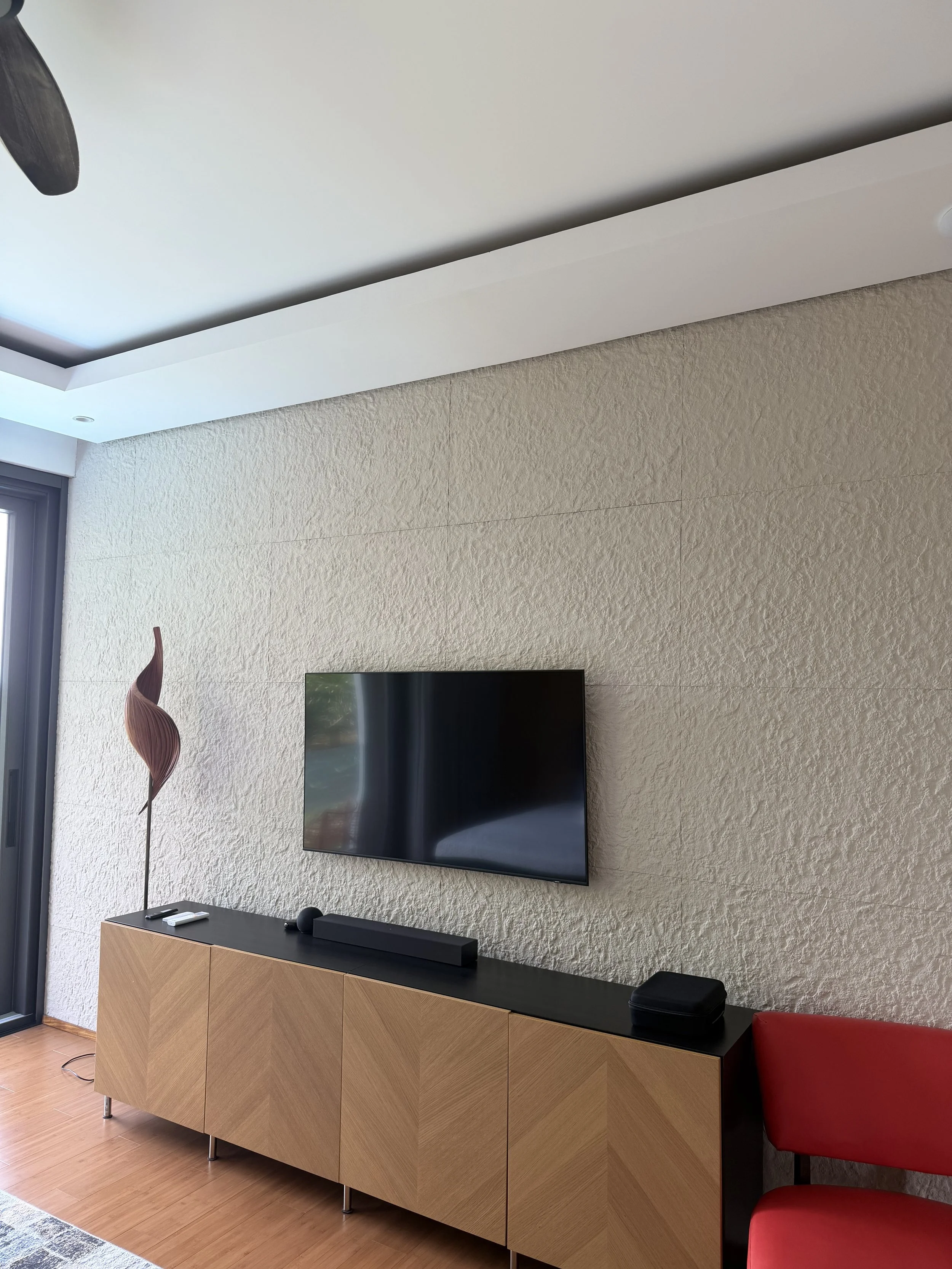 Living room with a wall-mounted TV, a wooden sideboard, a decorative sculpture, and a red chair.