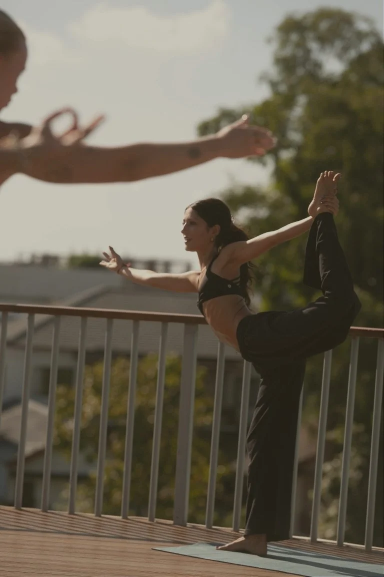 Woman practicing yoga on a balcony with another person offering support or coaching for been busy retreats