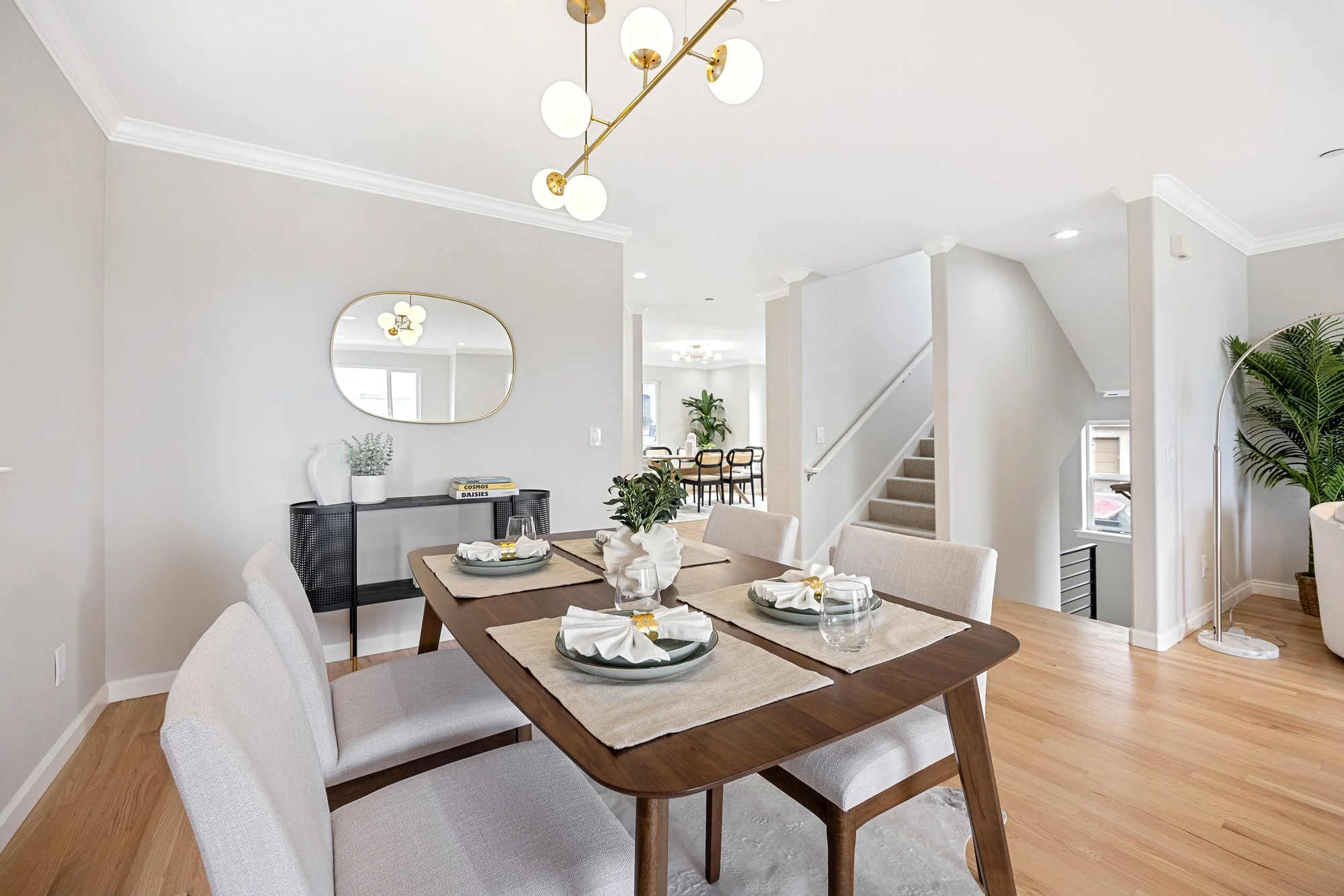 Staged dining area with wood table, neutral chairs, and open view to staircase and living space in renovated home