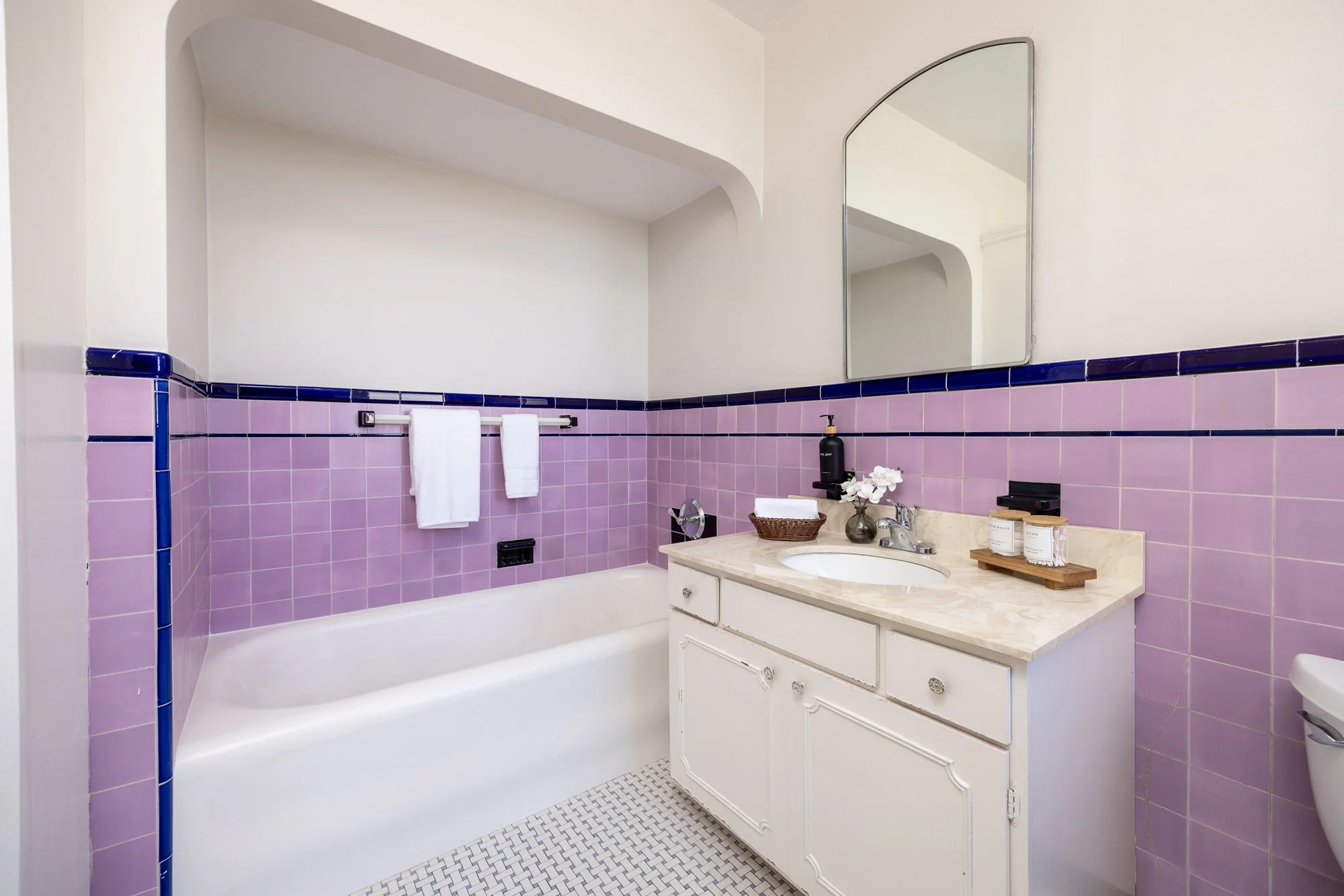 Vintage bathroom with pink tile walls, white vanity, and bathtub