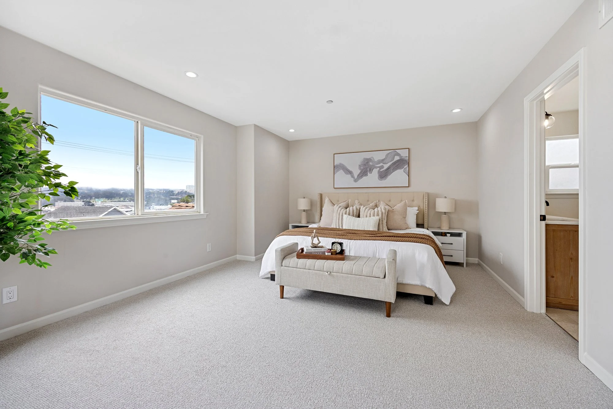 Staged bedroom with upholstered bed, neutral bedding, bedside lamps, and warm natural light