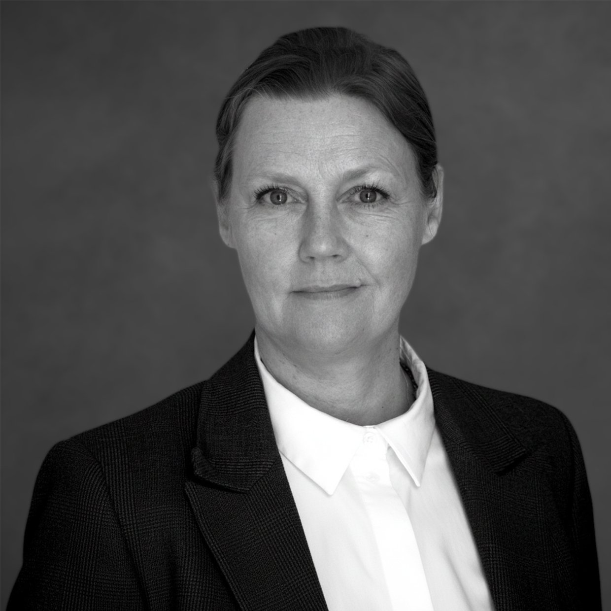 A black and white professional headshot of a woman with short hair, wearing a dark blazer and a white collared shirt, against a plain background.