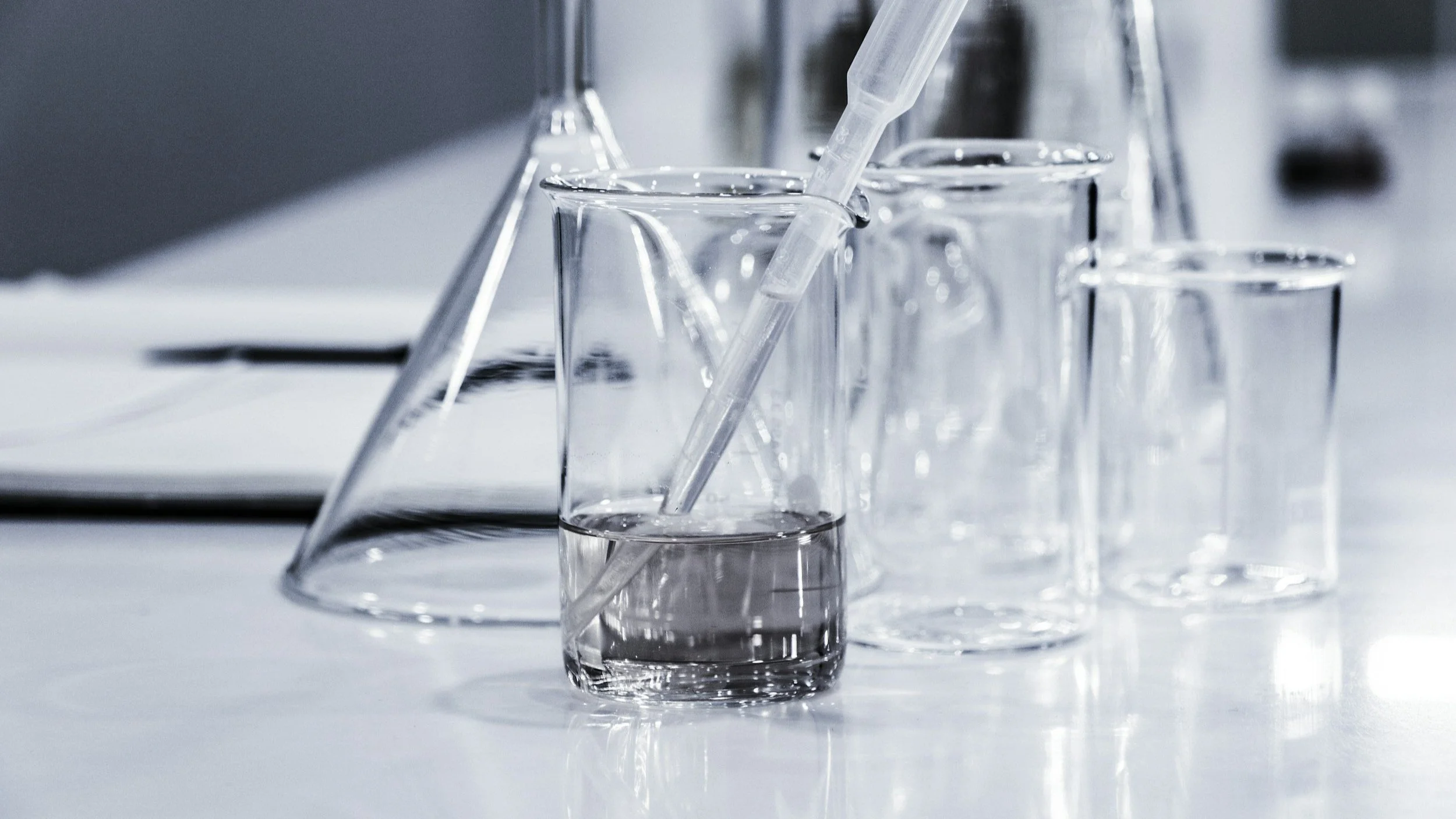 Laboratory glassware including test tubes, beaker with liquid, and pipette on a white surface.