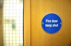 Blue circular fire door sign that says 'Fire door keep shut' on a yellow door.