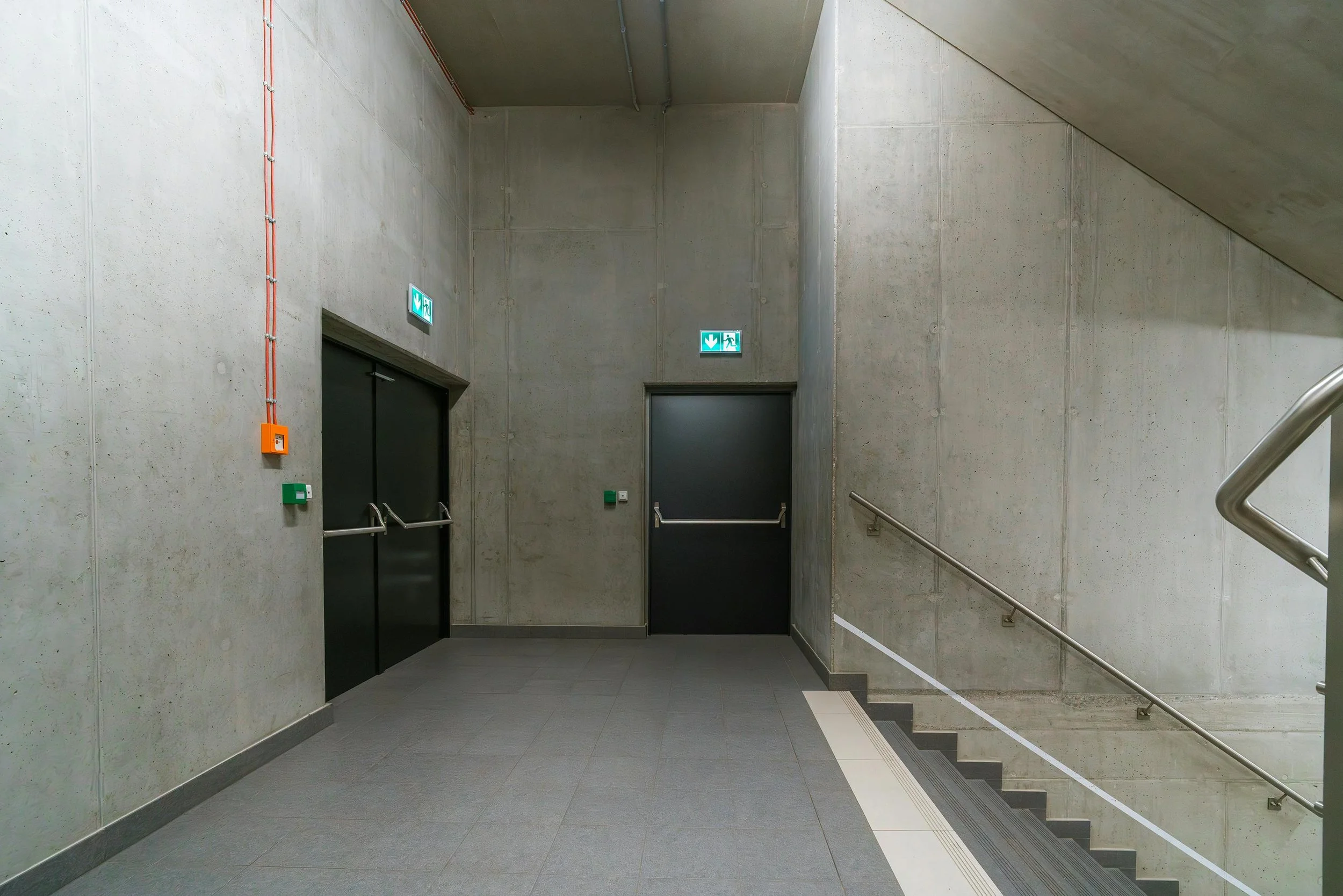 Concrete stairwell and emergency exit doors with illuminated exit signs in a modern building.