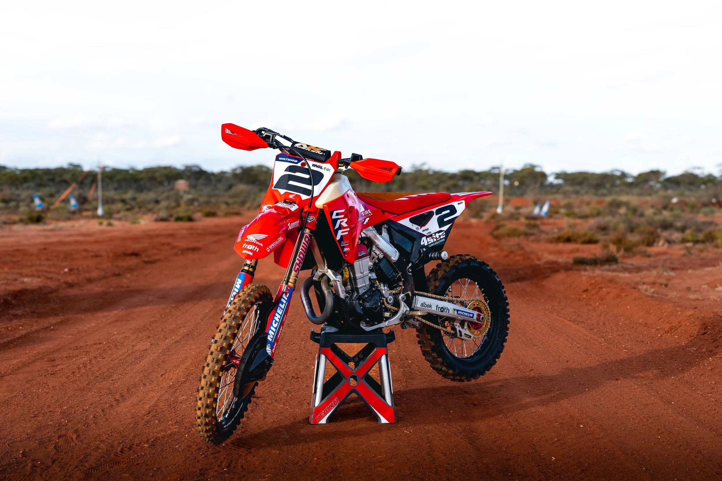 Red and white motocross bike on a dirt track in an arid landscape.