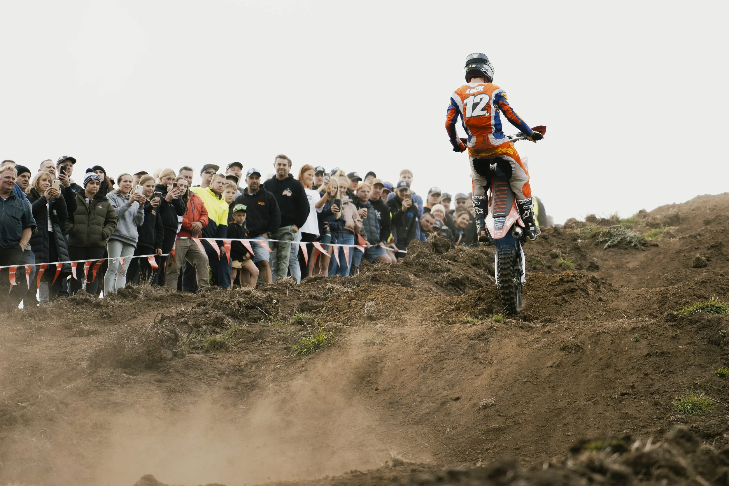 Motocross rider on dirt track with crowd watching from the side.