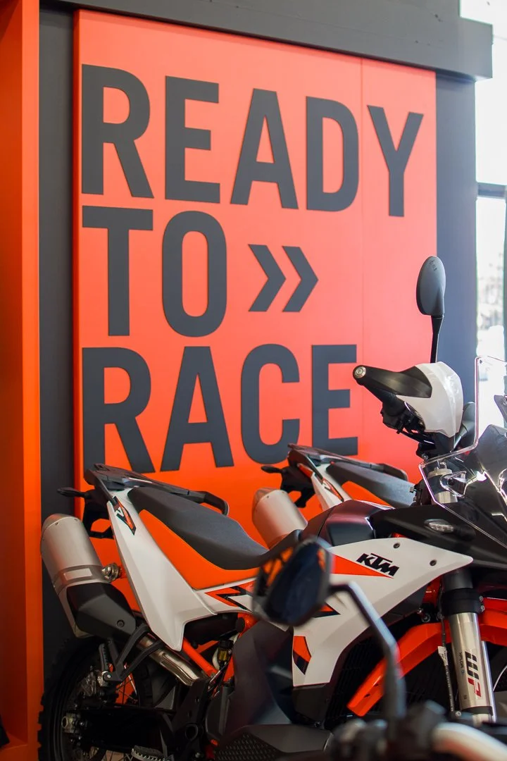 KTM motorcycles parked in front of a red wall with large black text saying "Ready to Race".