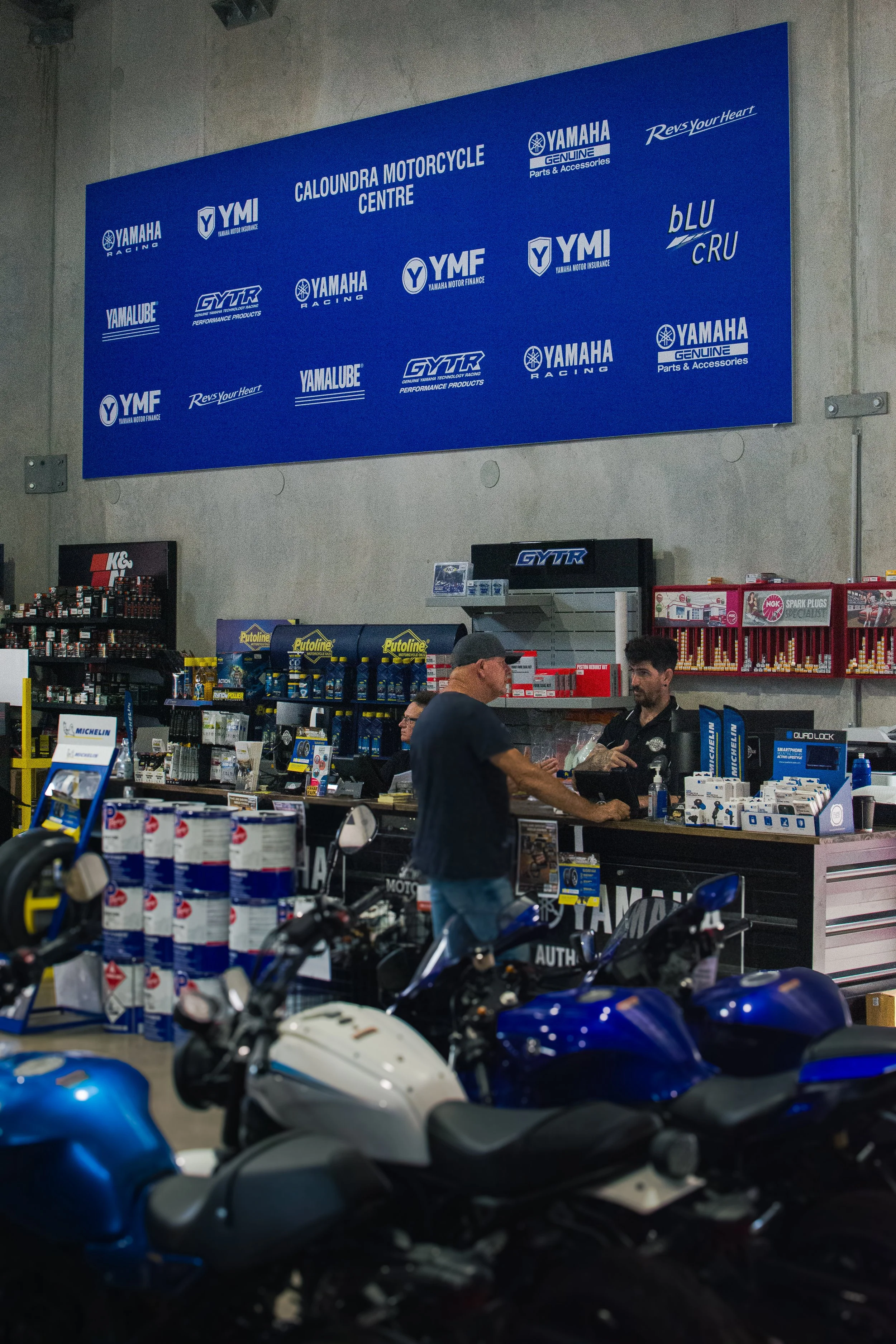 Inside Yamaha Caloundra Motorcycle Centre with motorcycles in foreground and staff assisting customer at counter in background.