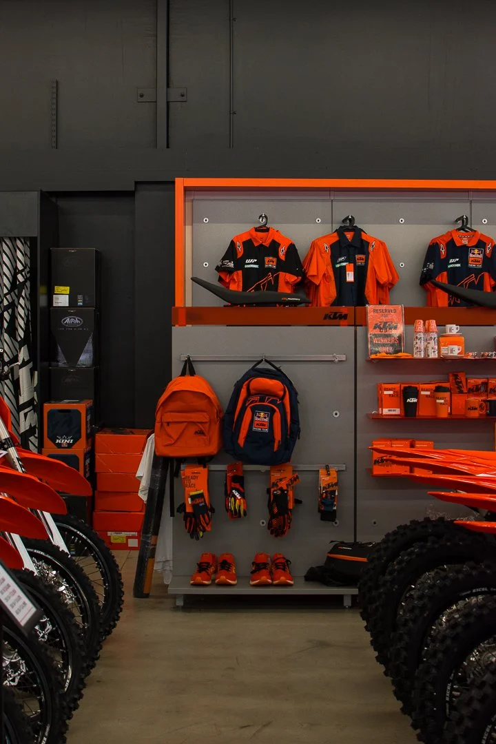 Display of KTM motorcycle racing gear and accessories, including jerseys, backpacks, gloves, shoes, and helmets in a hardware store.