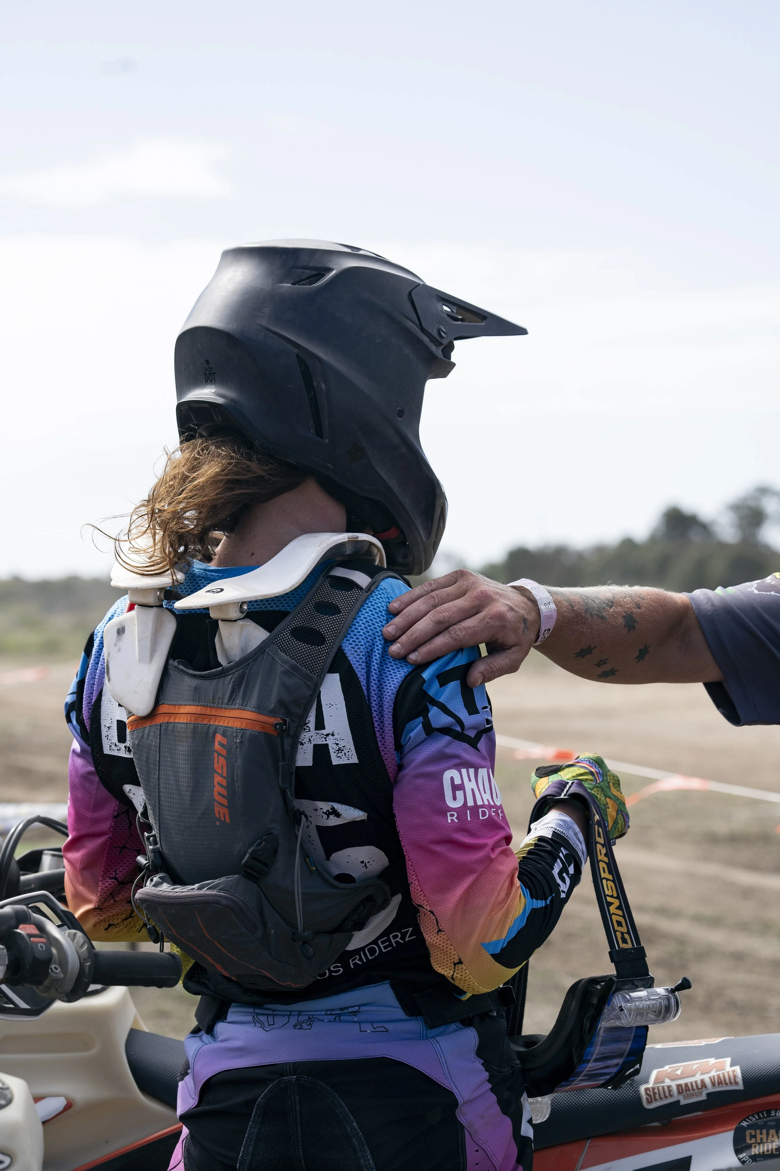 A motocross rider wearing a black helmet and a colorful jersey, being handed a handshake.