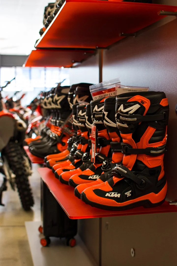A display of orange and black motocross boots on a red shelf in a store.