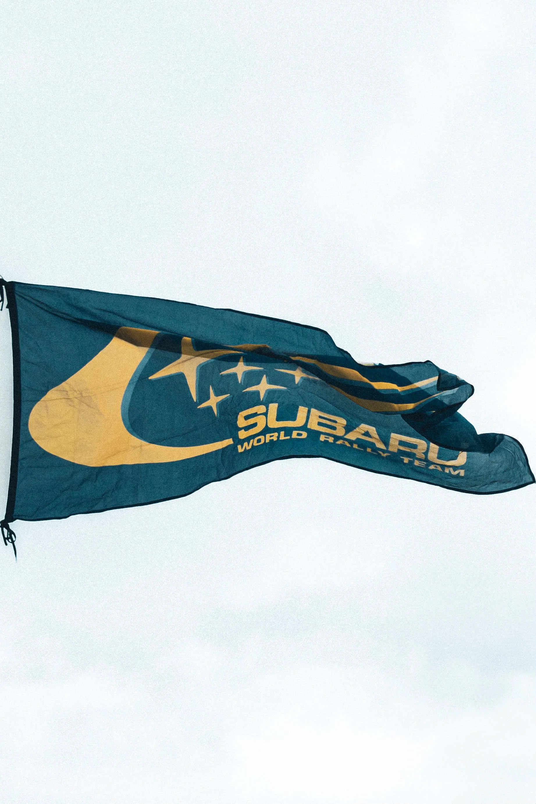 Subaru World Rally Team flag waving in the wind against a cloudy sky.