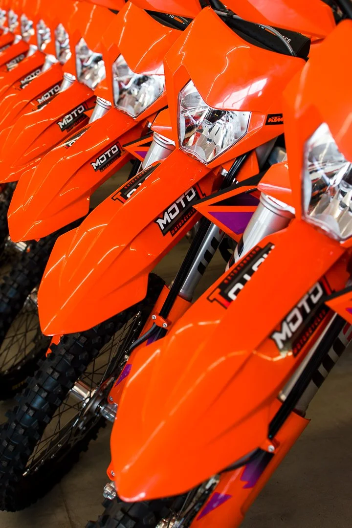 A row of orange KTM dirt bikes with black tires and front suspension forks.