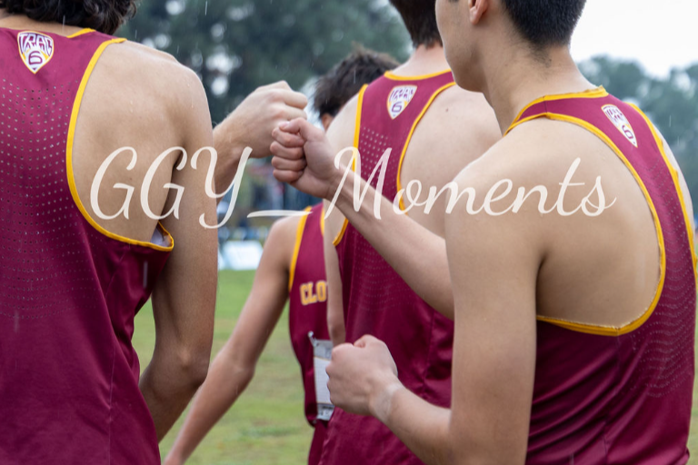 A group of young male athletes in maroon and gold sports uniforms giving each other a fist bump outdoors.