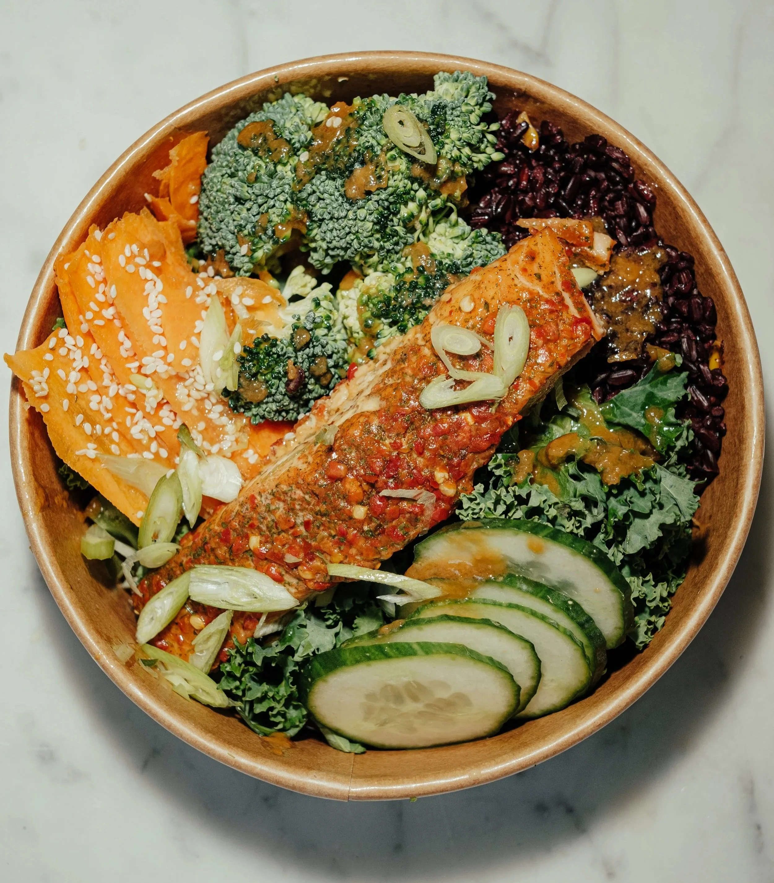 Greens & Grains salad bowl. Bowl of assorted salads with broccoli, carrots, and cucumber slices.