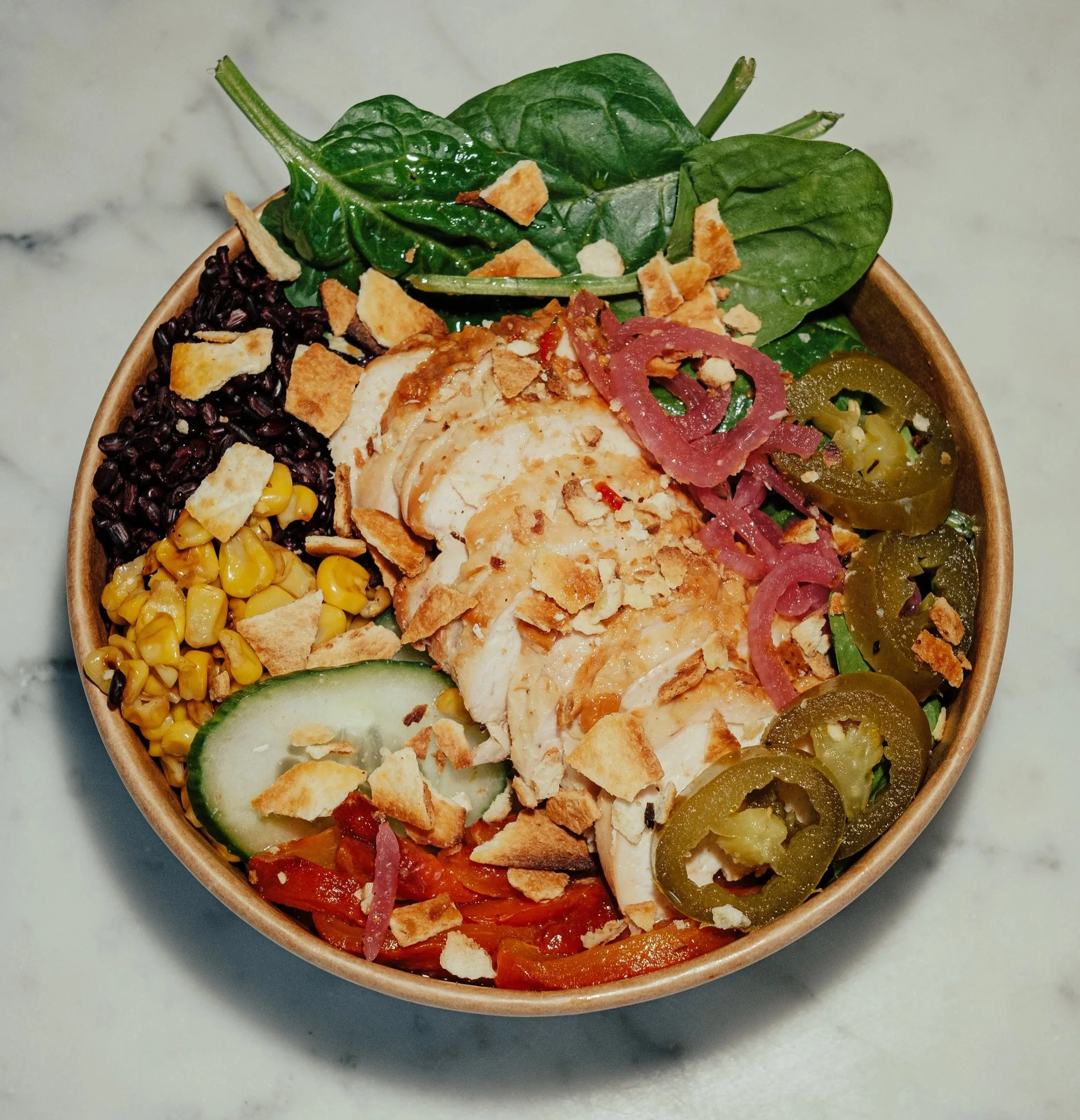 Greens & Grains salad bowl. Close-up of a bowl filled with a salad consisting of greens, corn, black beans, sliced peppers, onions, and chicken, topped with crushed crackers.