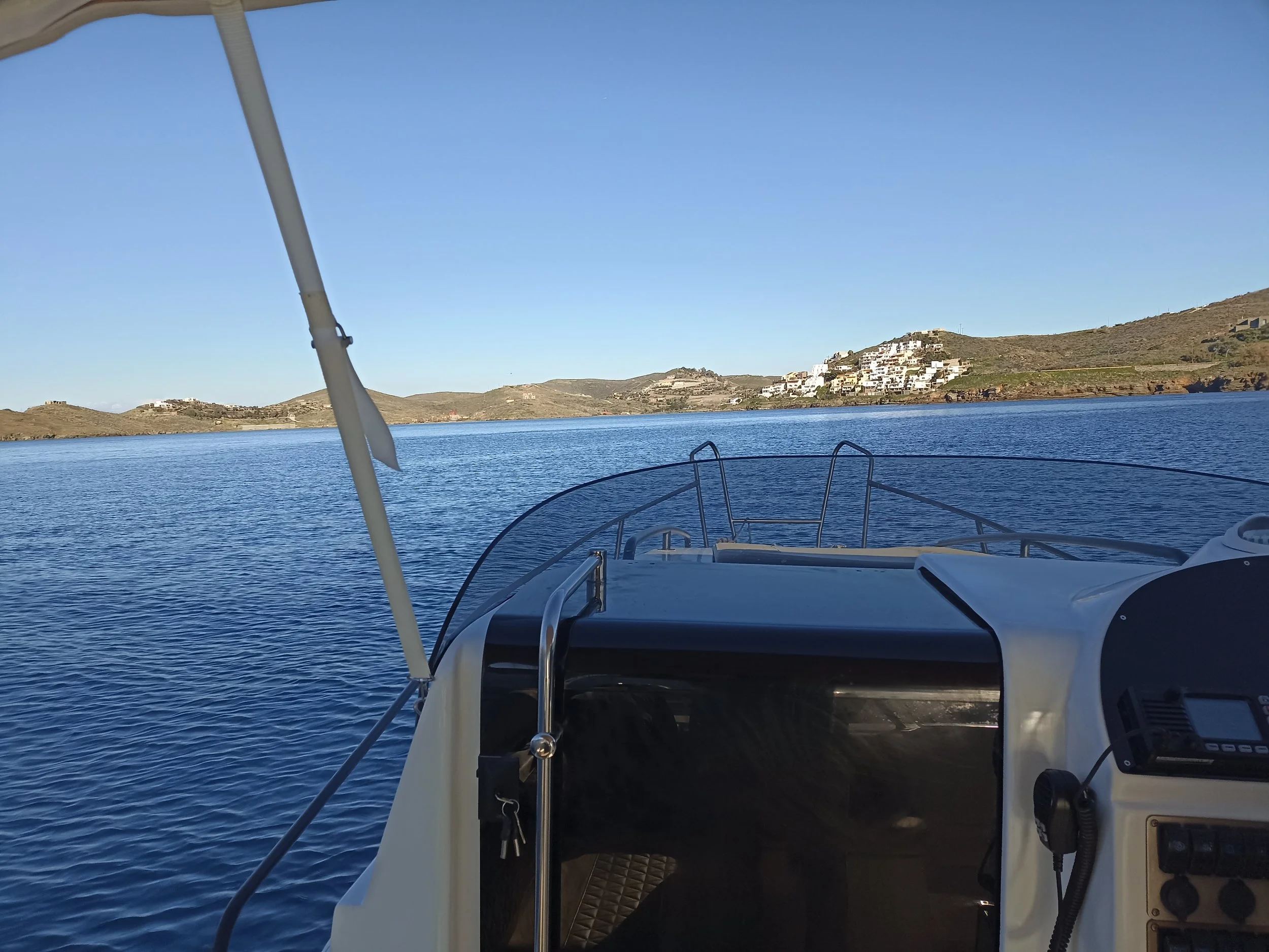 View from a boat looking towards a mountain with white buildings, calm blue water, and a clear sky.