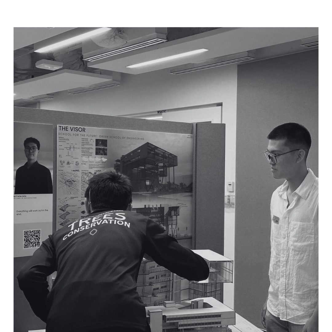 Two young men are presenting and examining a school project display about the Green School of Engineering. One man is reading notes, while the other stands nearby, paying attention.