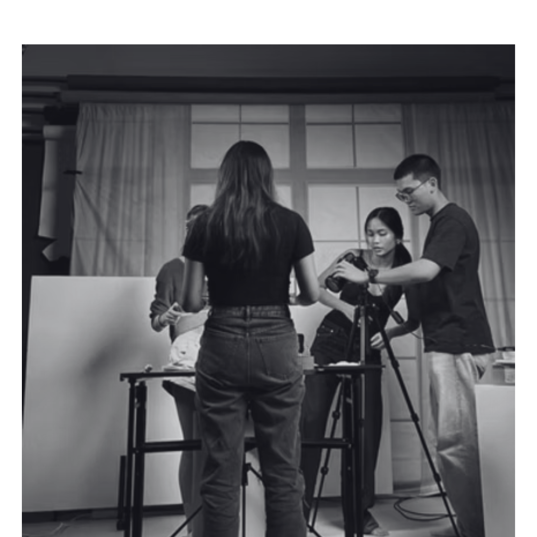 Four people in a room setting up or working on a camera, with a large window and curtains in the background.