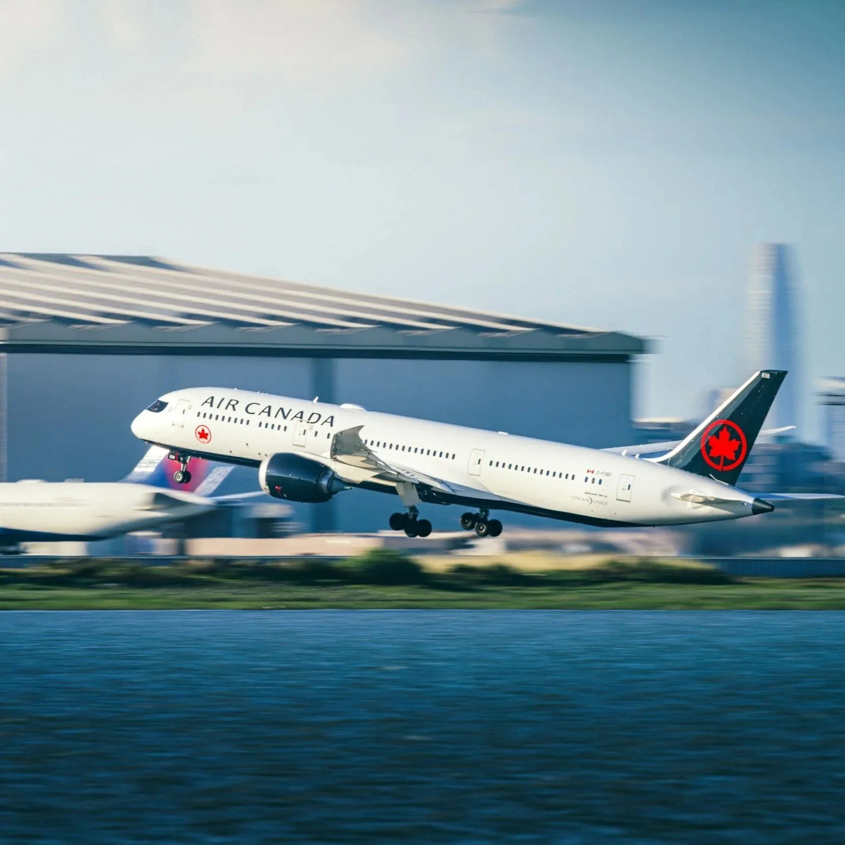 An Air Canada airplane taking off from a runway with a cityscape and skyscrapers in the background.