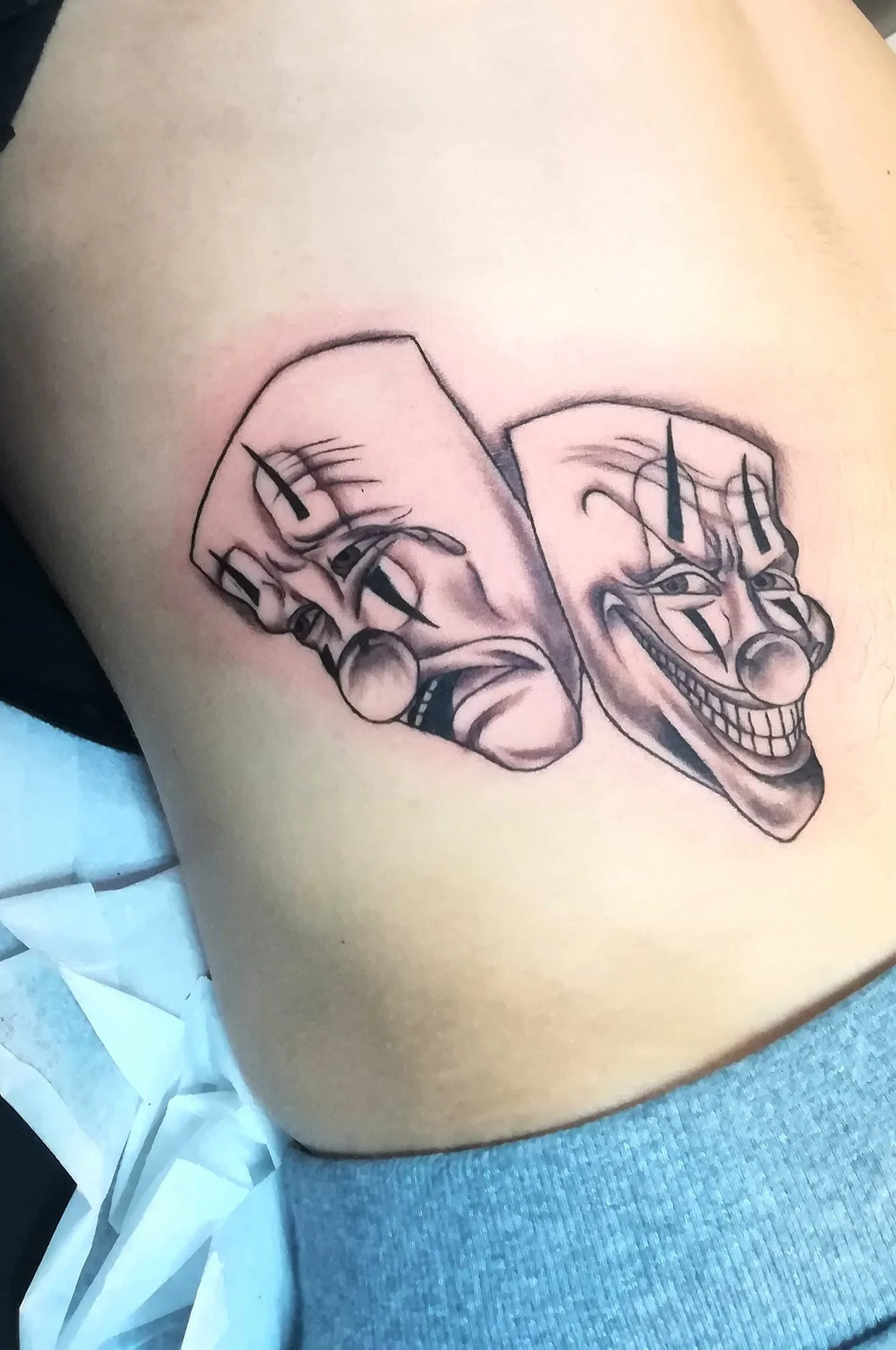 Dviejų kaukių (verkiančios ir besišypsančios) tatuiruotė ant krūtinės.