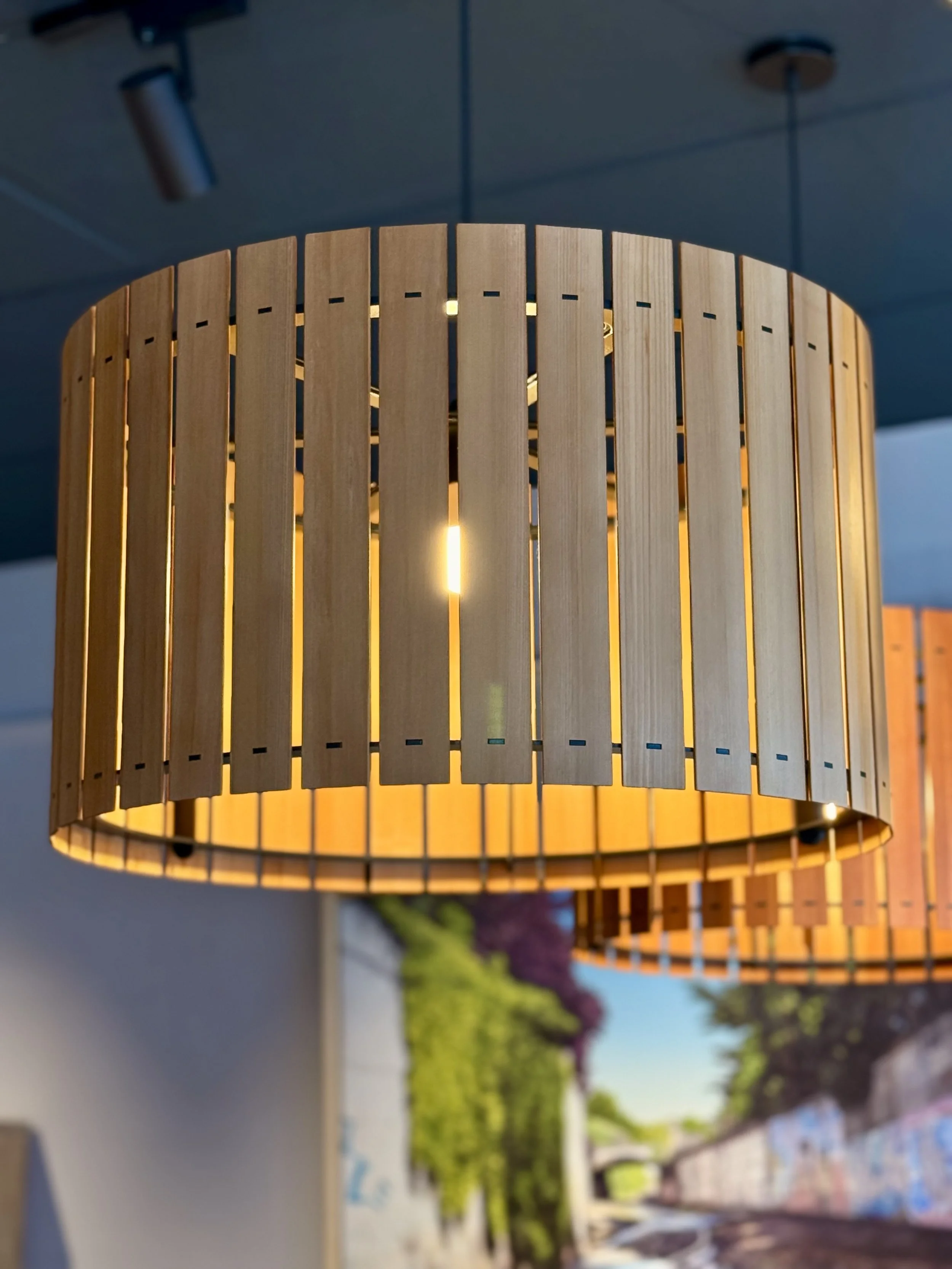 Wooden cylindrical pendant lamp hanging from ceiling, with warm interior lighting, in a modern interior space.