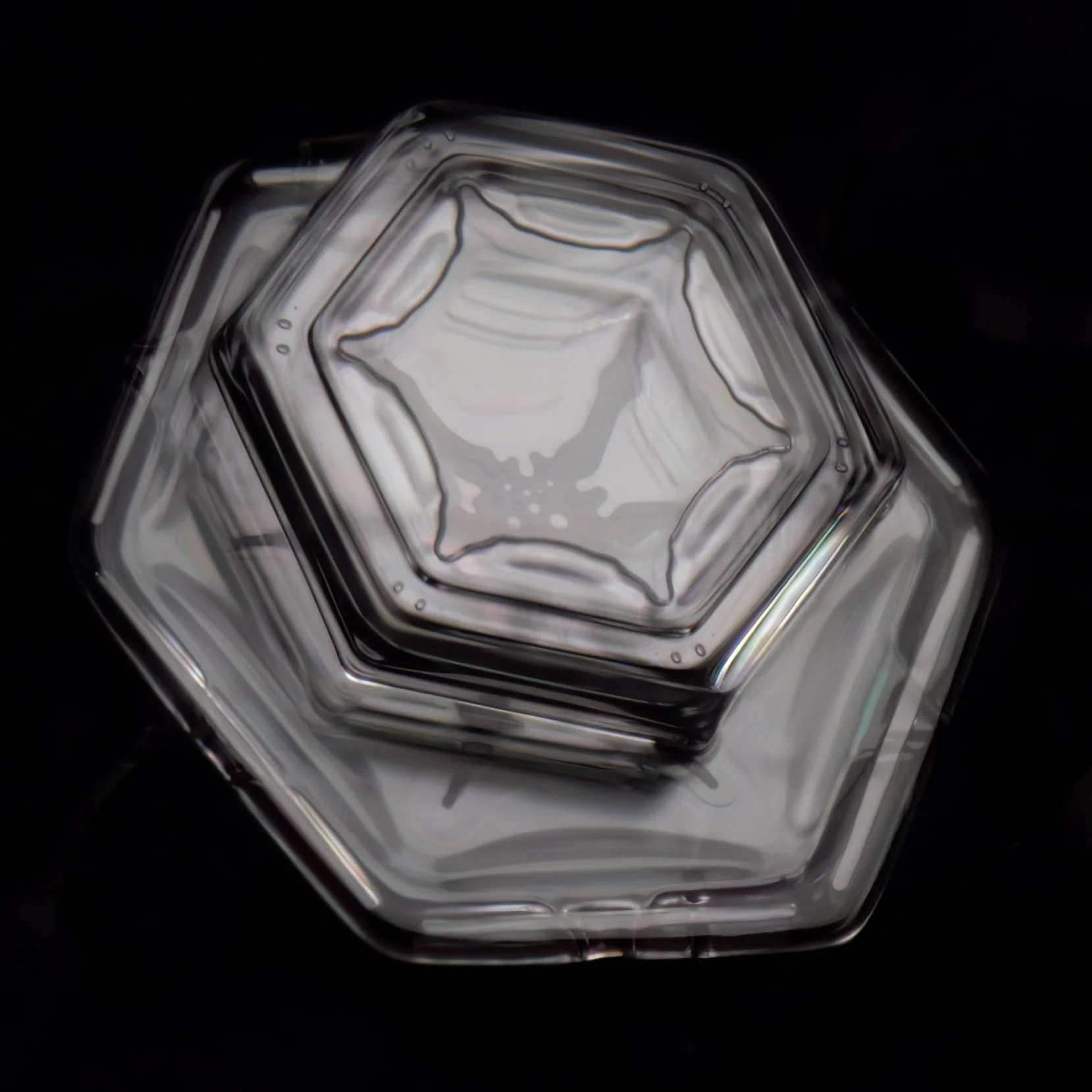 Macro photograph of two clear glassy hexagon-shaped snow crystals, viewed from above against a black background.
