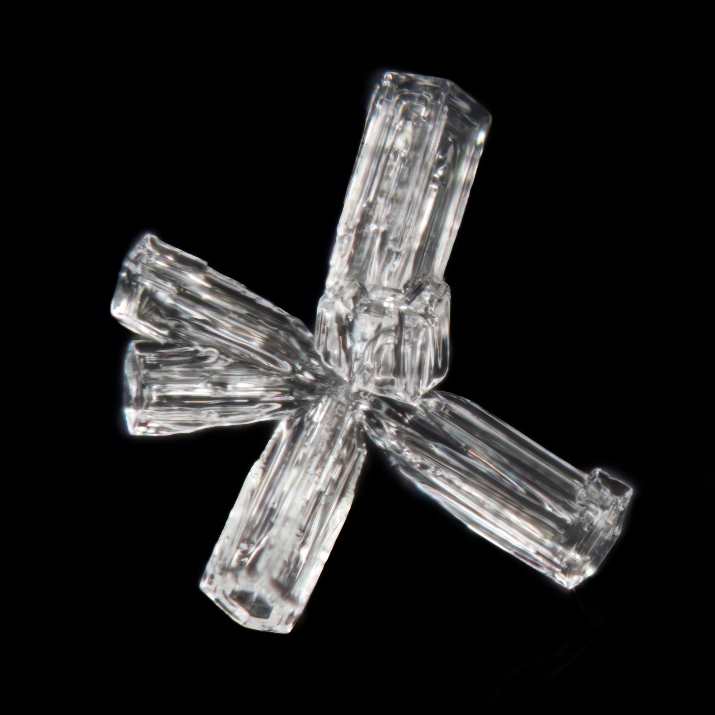 Macro photograph of a clear, faceted irregular snow crystal with thin extension.