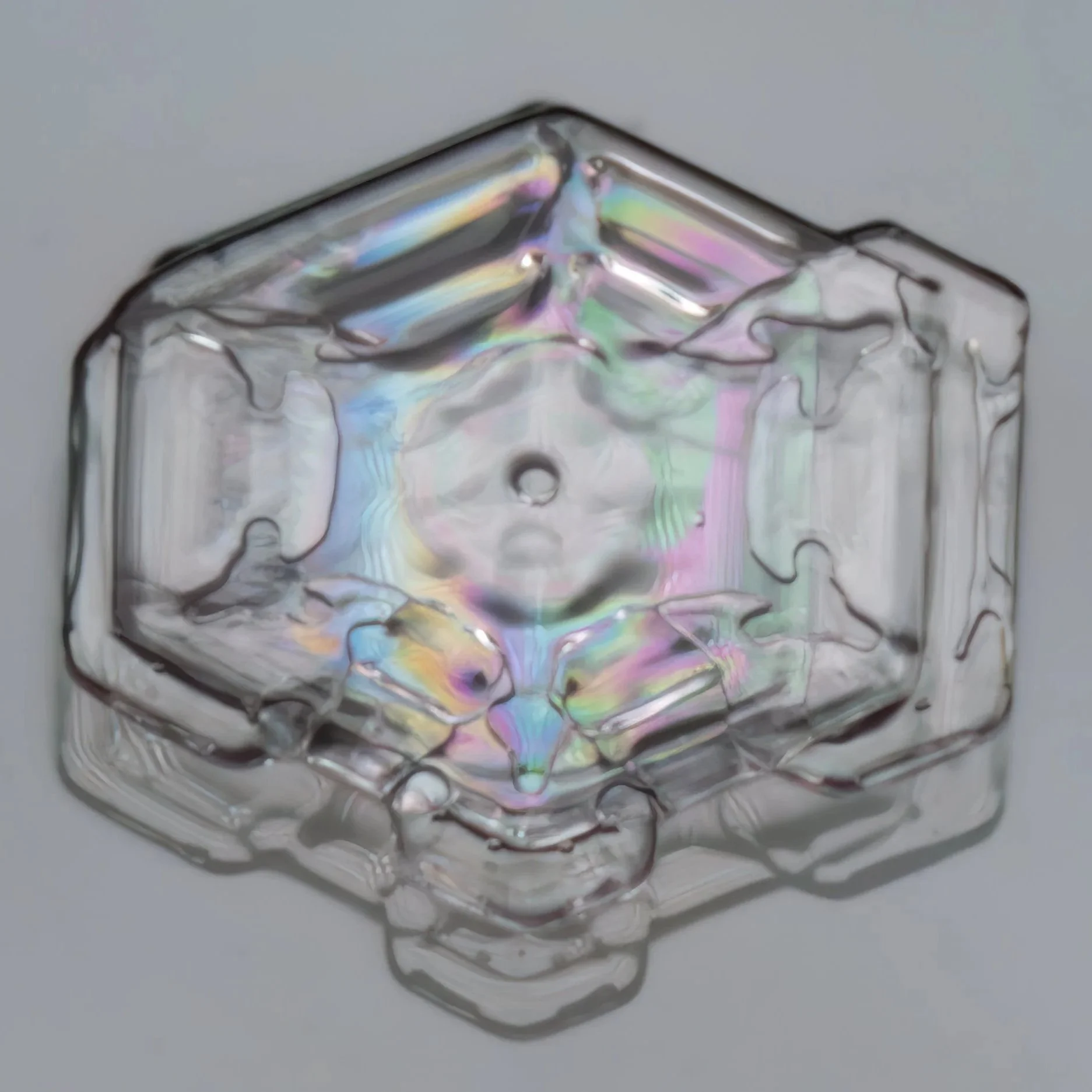 Macro photograph of a small plate-shaped snow crystal with rainbow-like reflections from thin film interference.