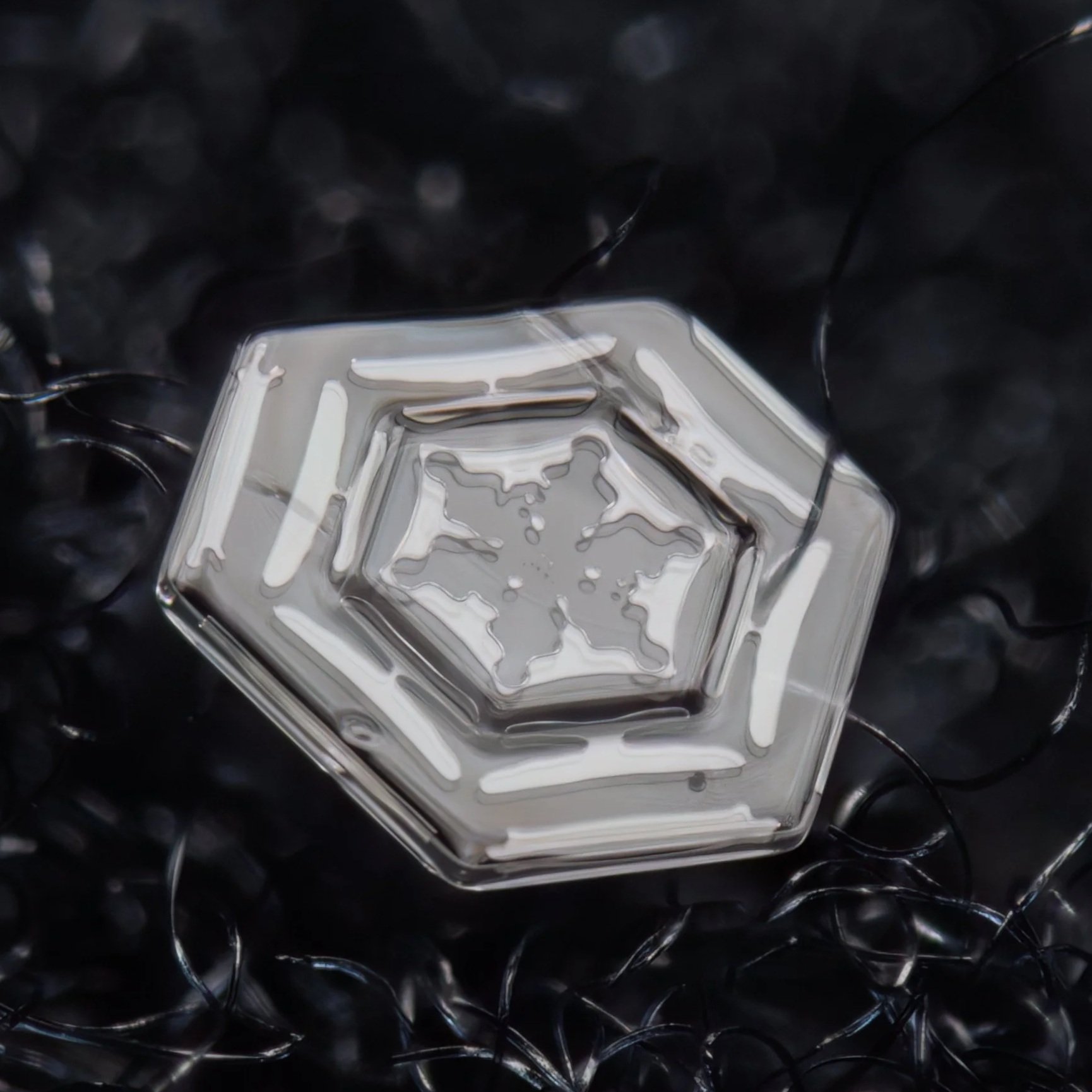Macro photograph of a hexagonal snow crystal with a star-shaped pattern inside.