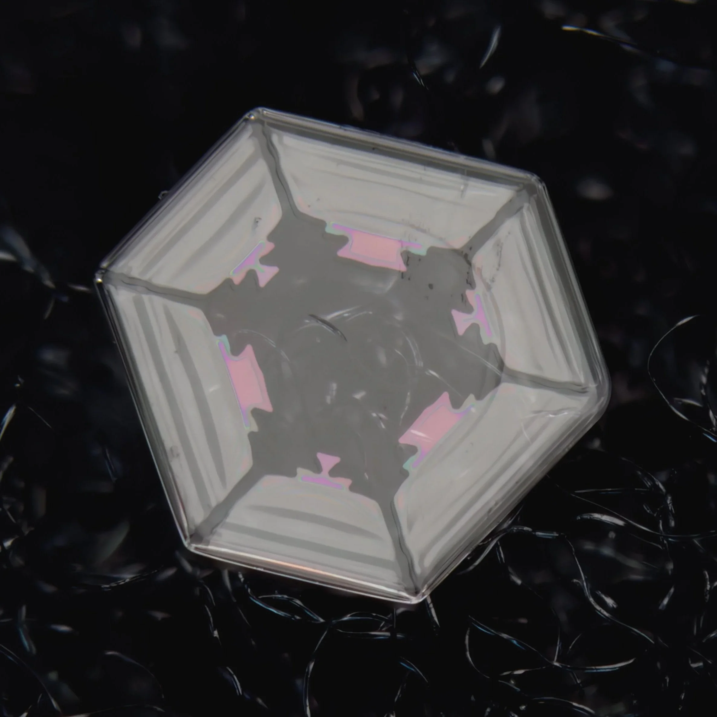 Macro photograph of a transparent, hexagonal-shaped, snow crystal with iridescent edges.