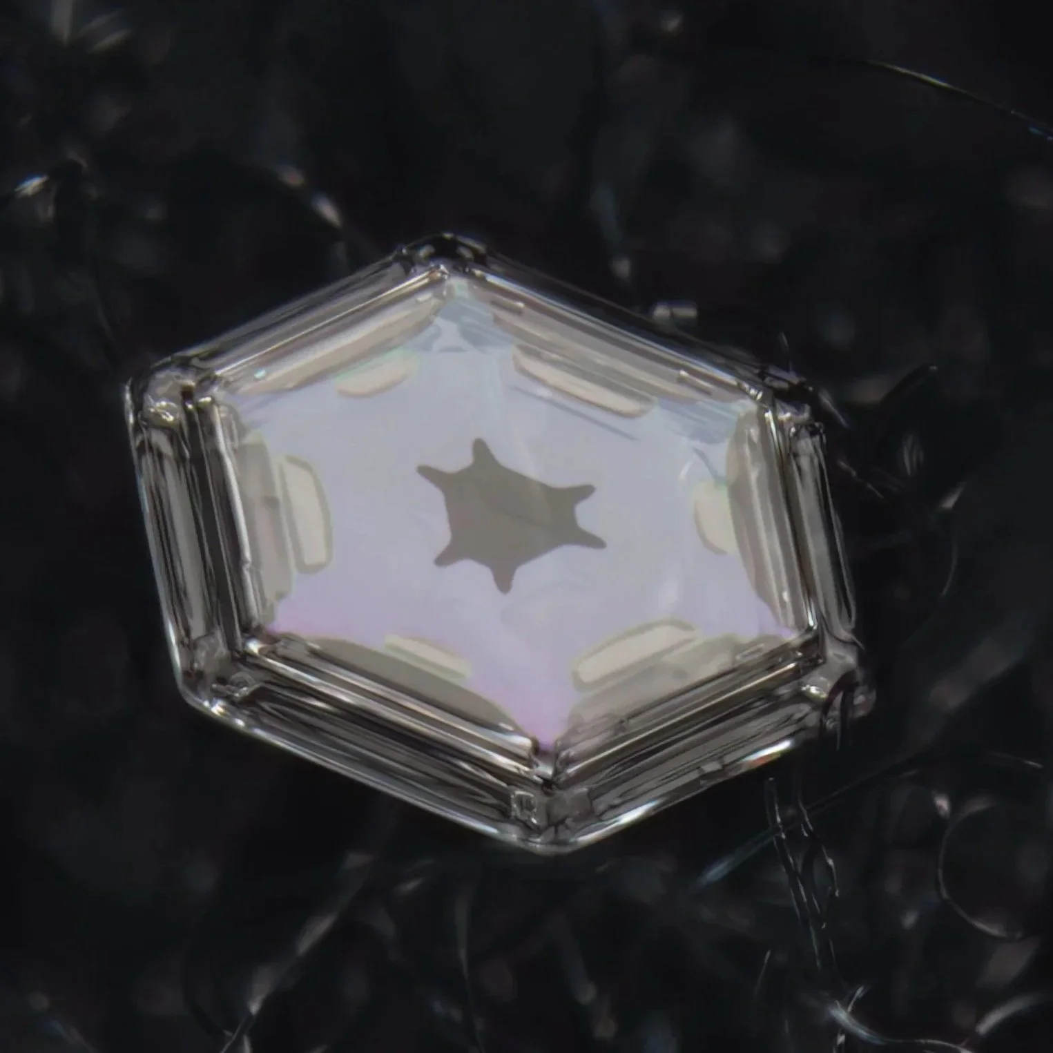 Macro photograph of a very small snowflake in a hexagonal shape, reflecting light against a dark background.