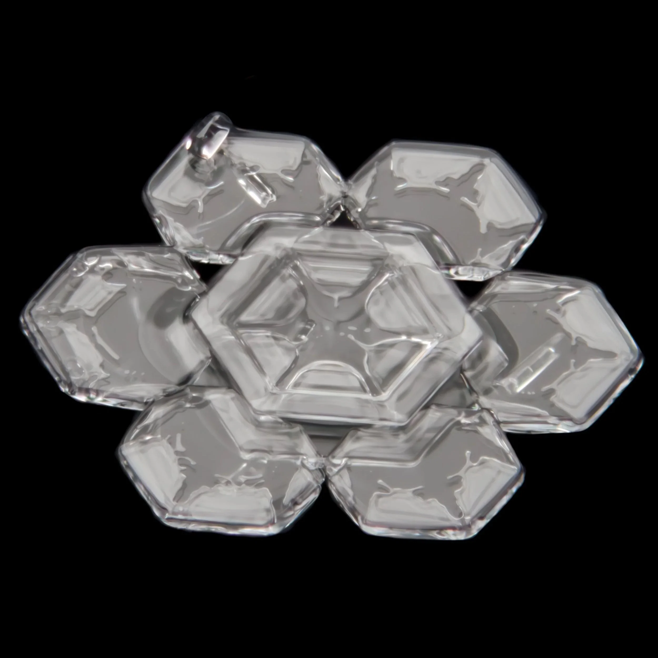 Macro photograph of a clear glassy snow crystal with geometric patterns, arranged in a symmetrical flower-like configuration.