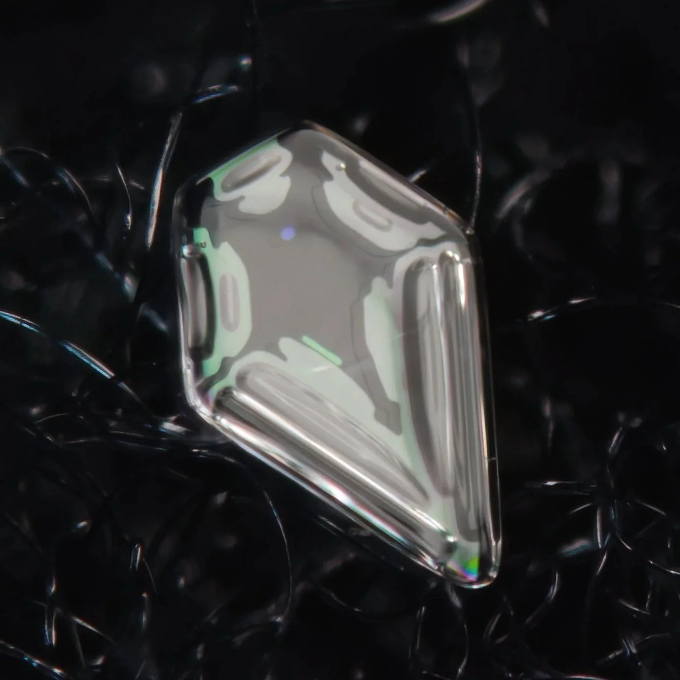 Macro photograph of a clear, shiny, irregularly shaped snow crystal.