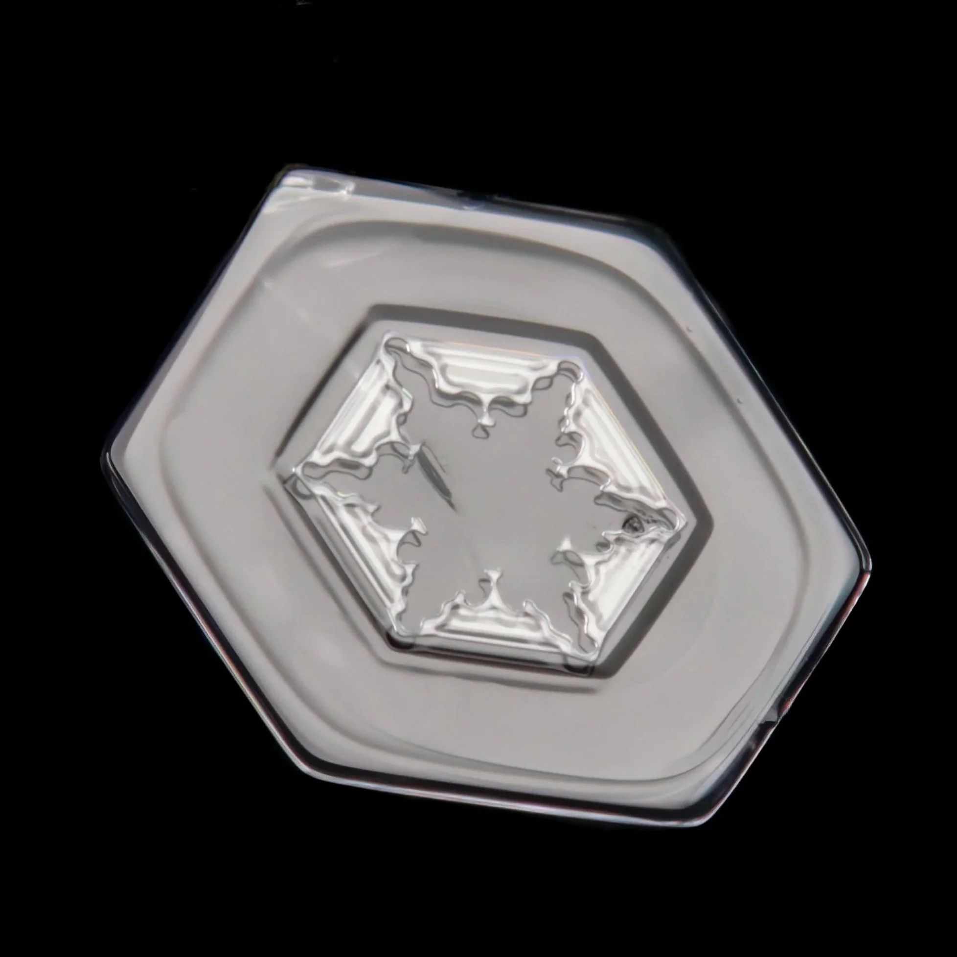 Macro photograph of a small plate snowflake with a starlike pattern in the center part.