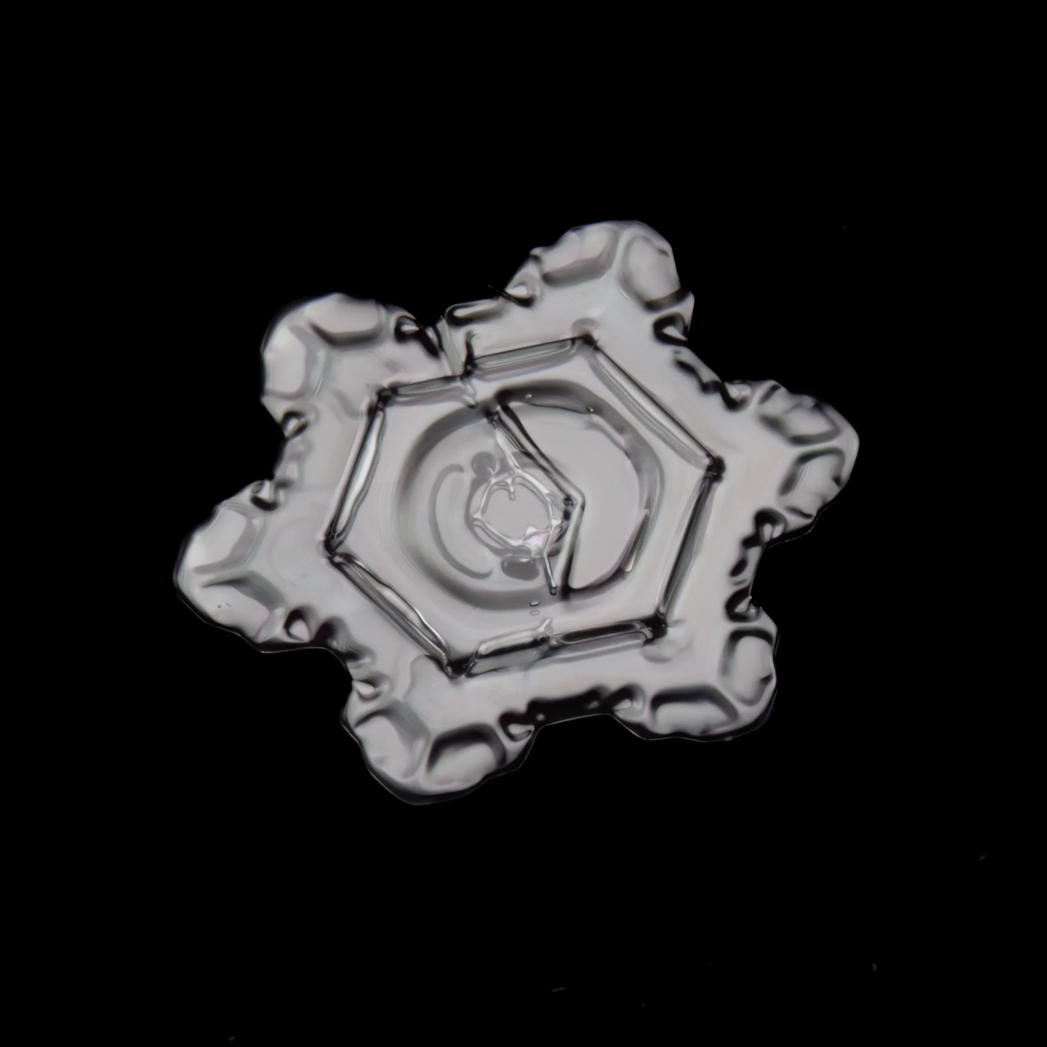 Macro photograph of a sectored plate snowflake with a hexagonal pattern in the center.