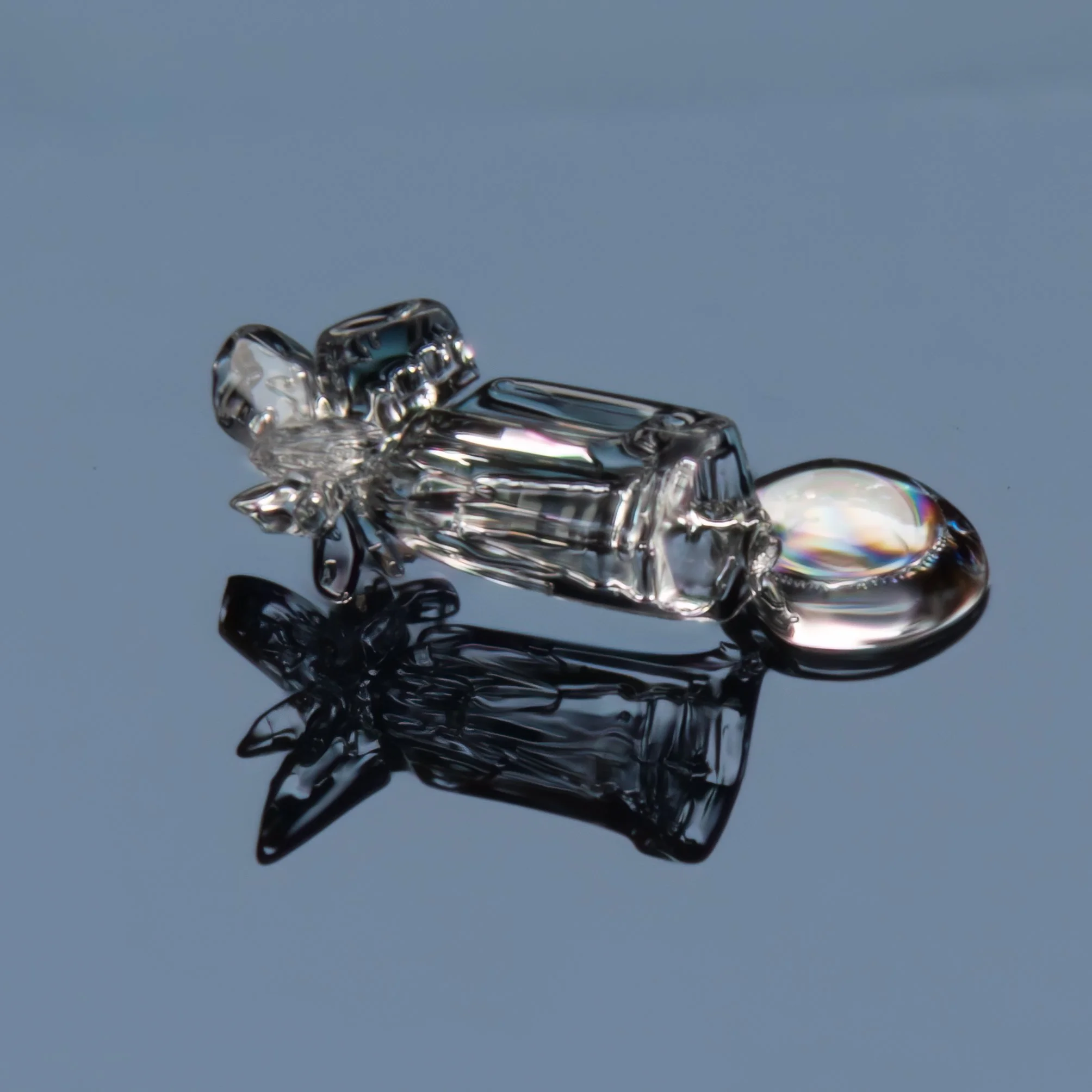 Macro photograph of a clear irregular snow crystal on a reflective surface.