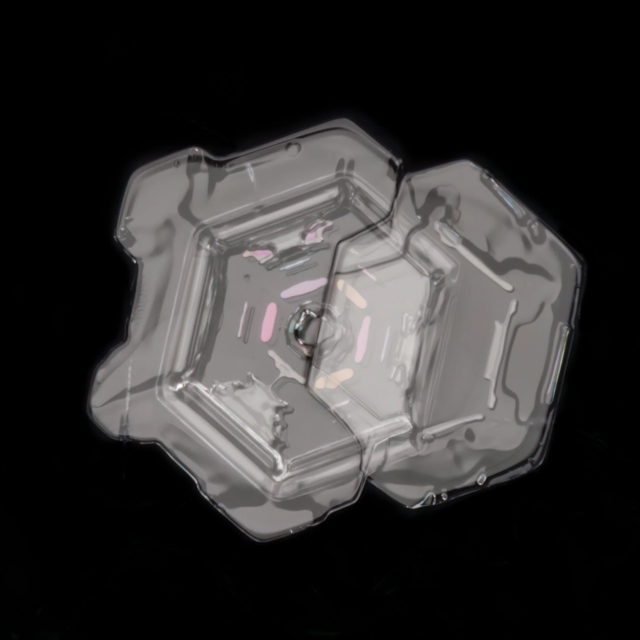 Macro photograph of a small irregular snow crystal with colourful center patterns from thin film interference.