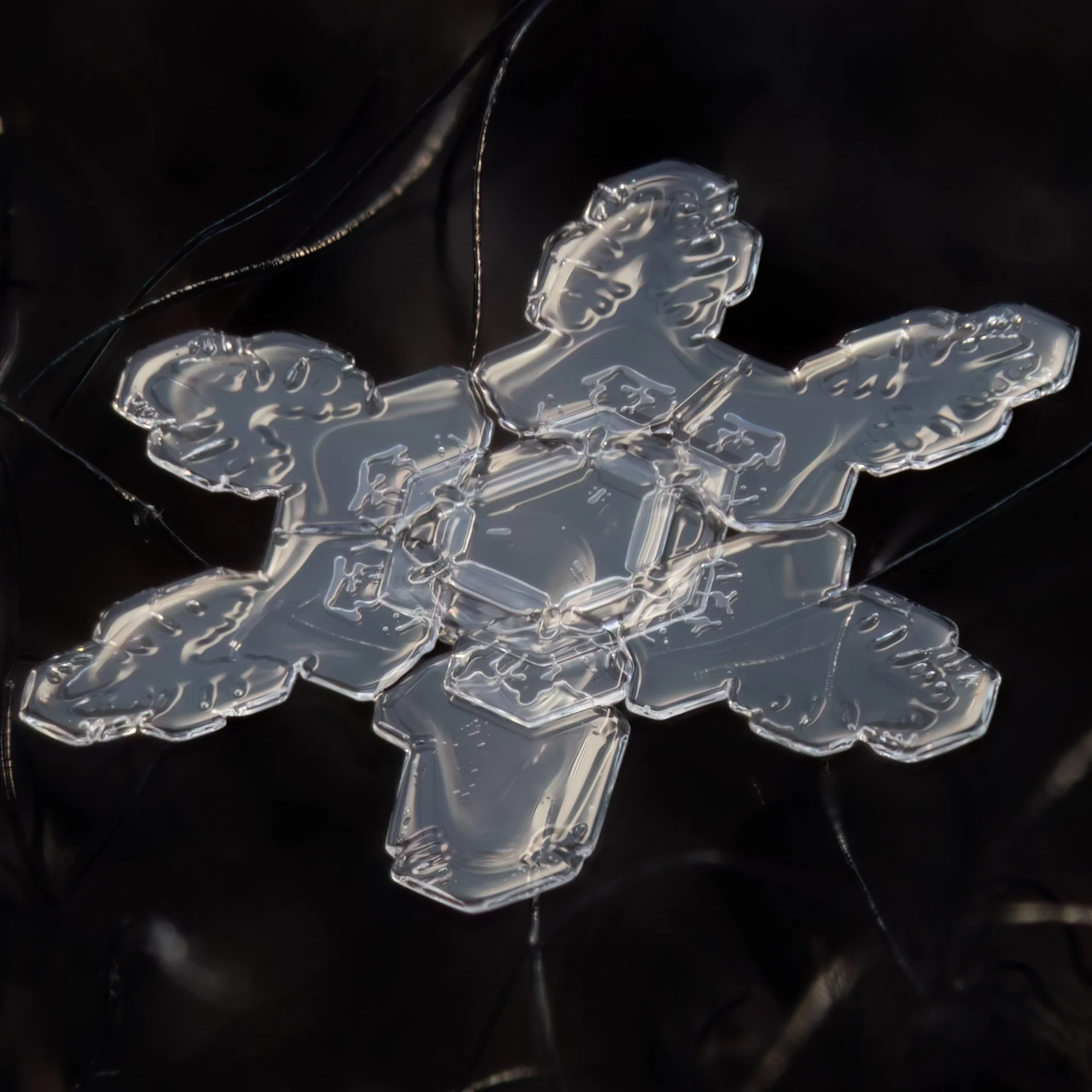 Macro photograph of a clear glassy snowflake with geometric center pattern.
