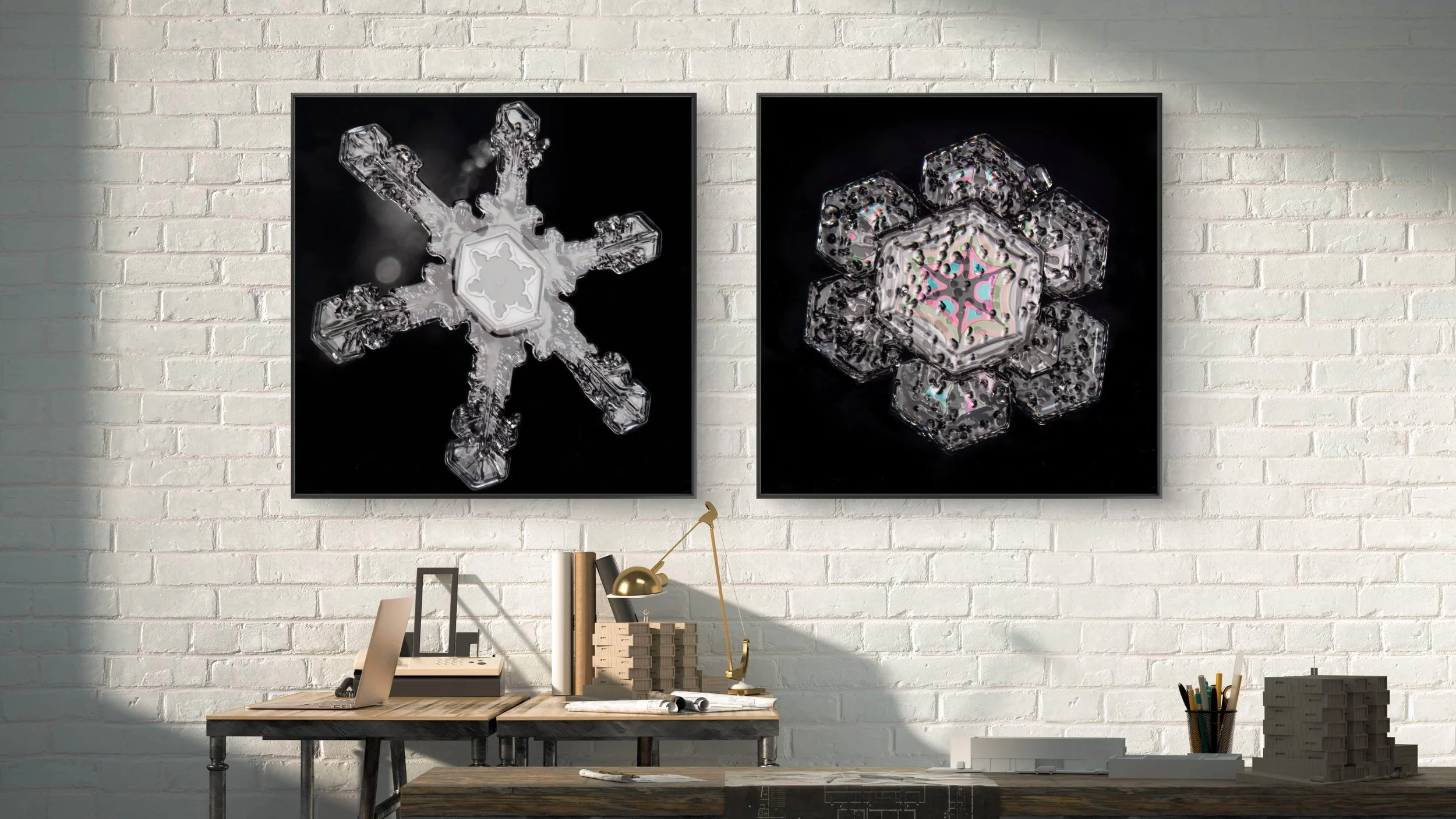Two framed photographs of detailed ice crystal snowflakes are hung on a white brick wall in a modern workspace. The workspace features a desk with books, a golden desk lamp, a laptop, and various office supplies.