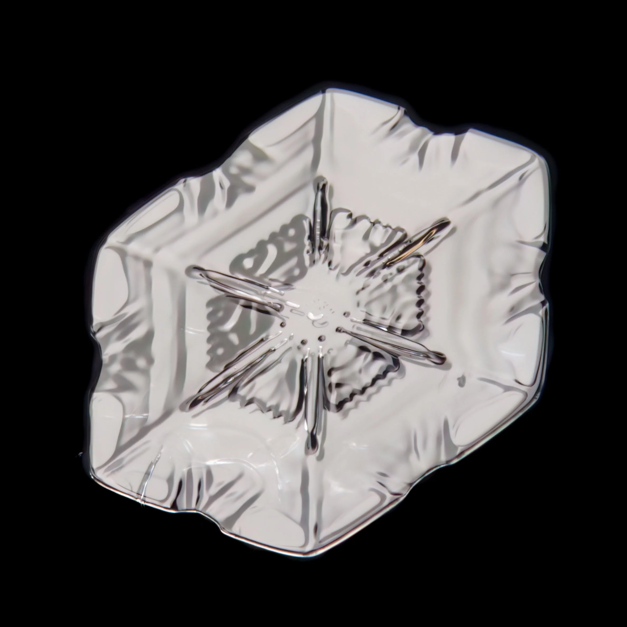 Macro photograph of a small plate snow crystal photographed in Oulu, Finland, with intricate pattern.