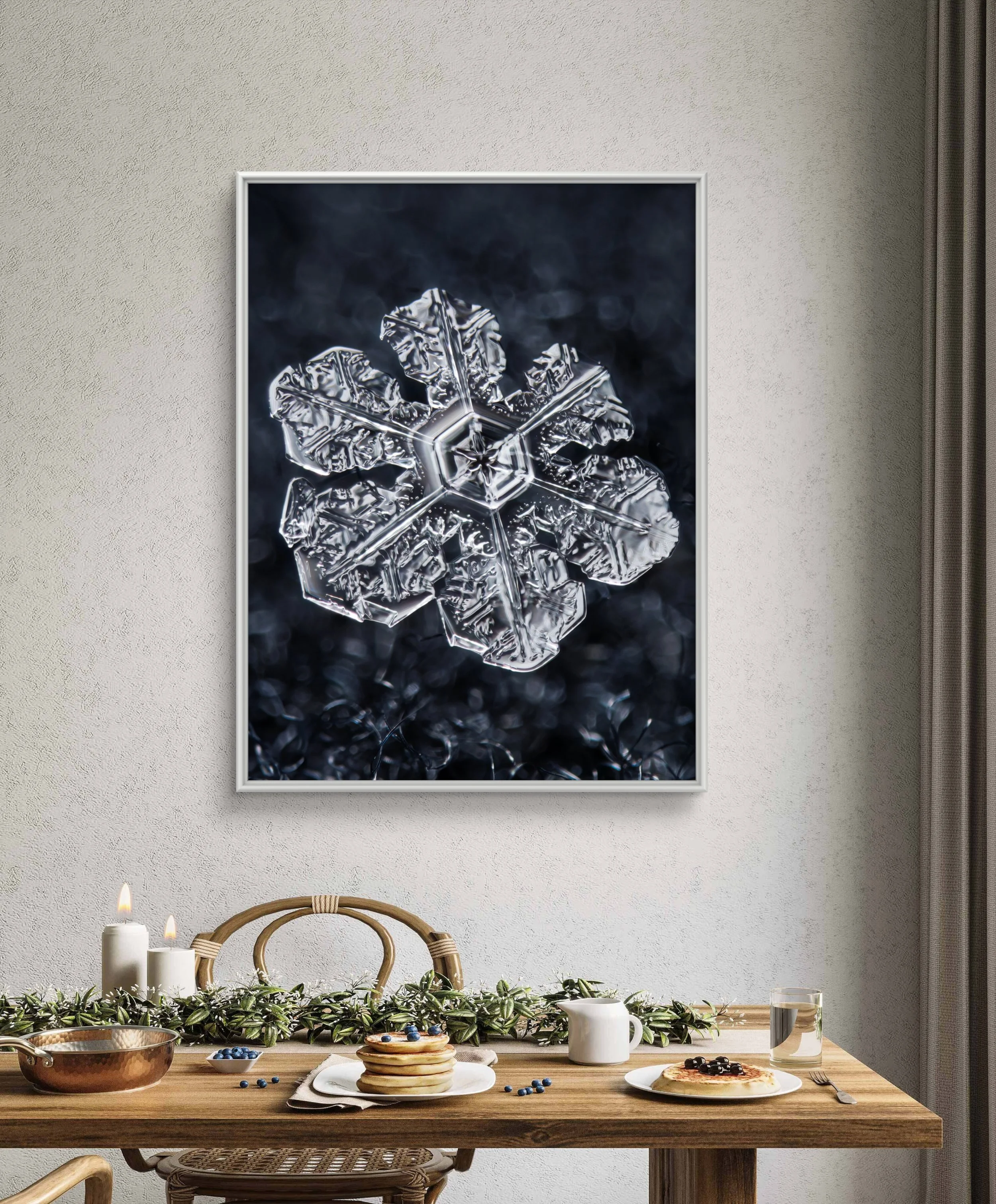 Close-up of a detailed snowflake on a dark background, framed and hung on a wall in a dining area with a wooden table, candles, pancakes, blueberries, and a glass of water.