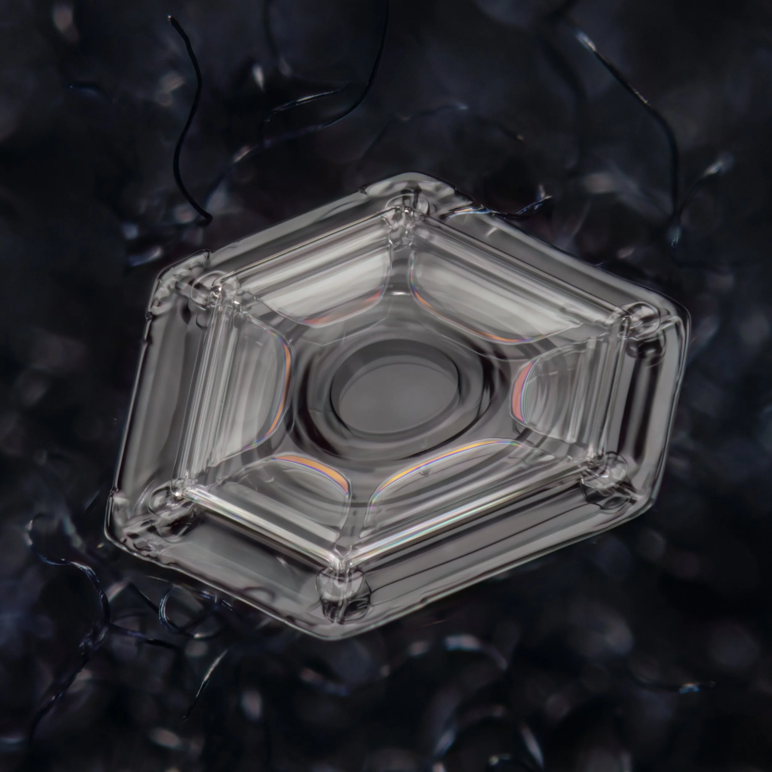 Macro photograph of a small plate shaped snow crystal with colours from thin film interference clearly visible.